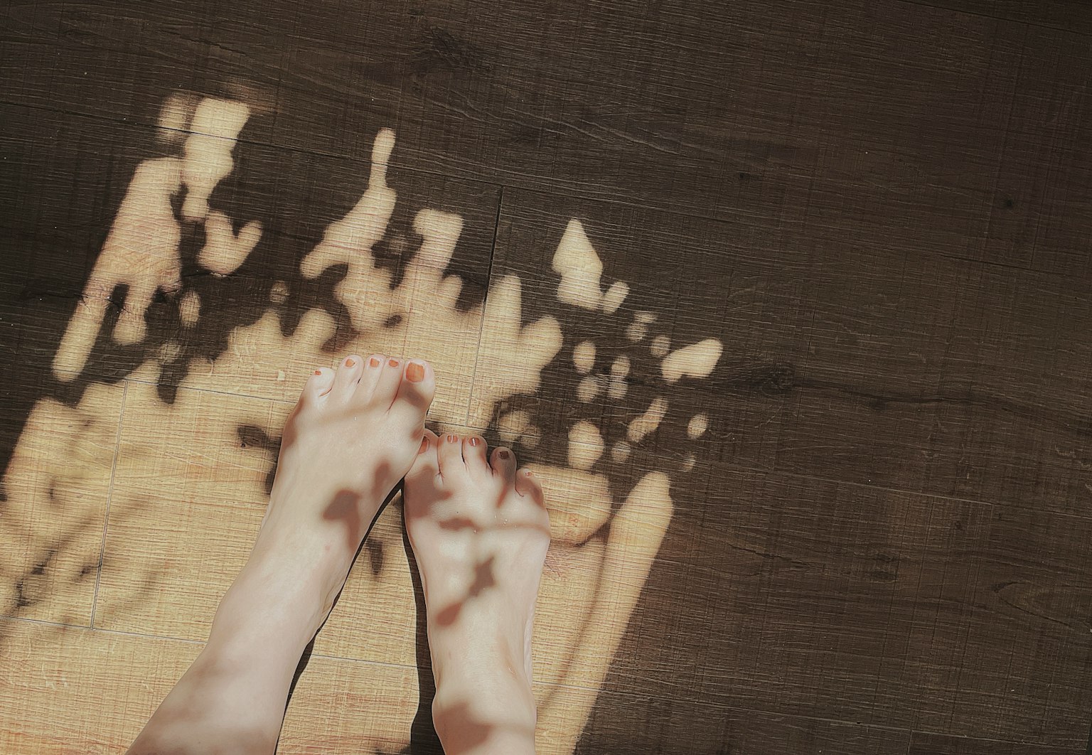 Pieds projetant des ombres sur un sol en bois avec de la lumière tamisée