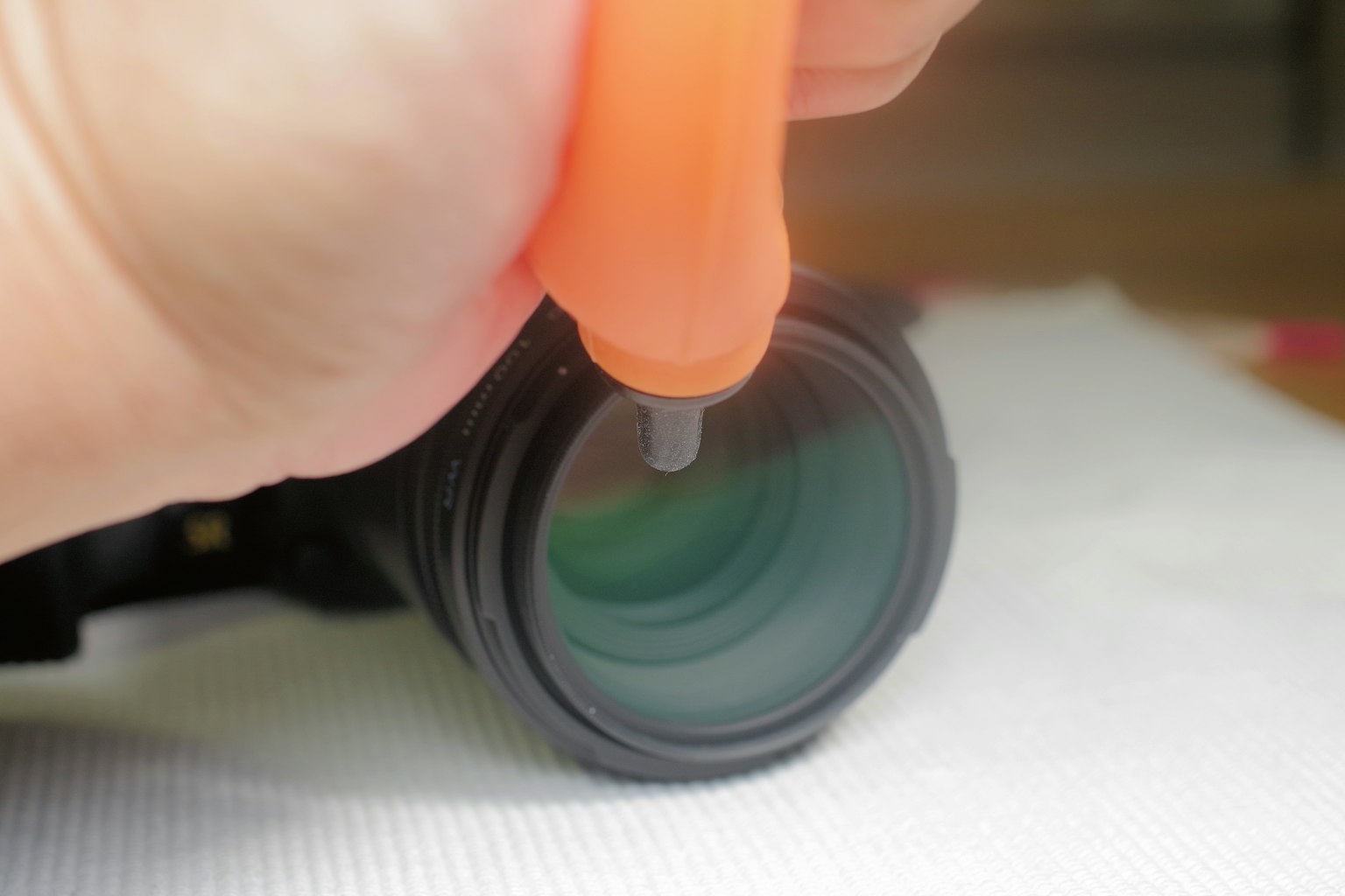 Primo piano di una mano che pulisce un obiettivo fotografico con un detergente per lenti