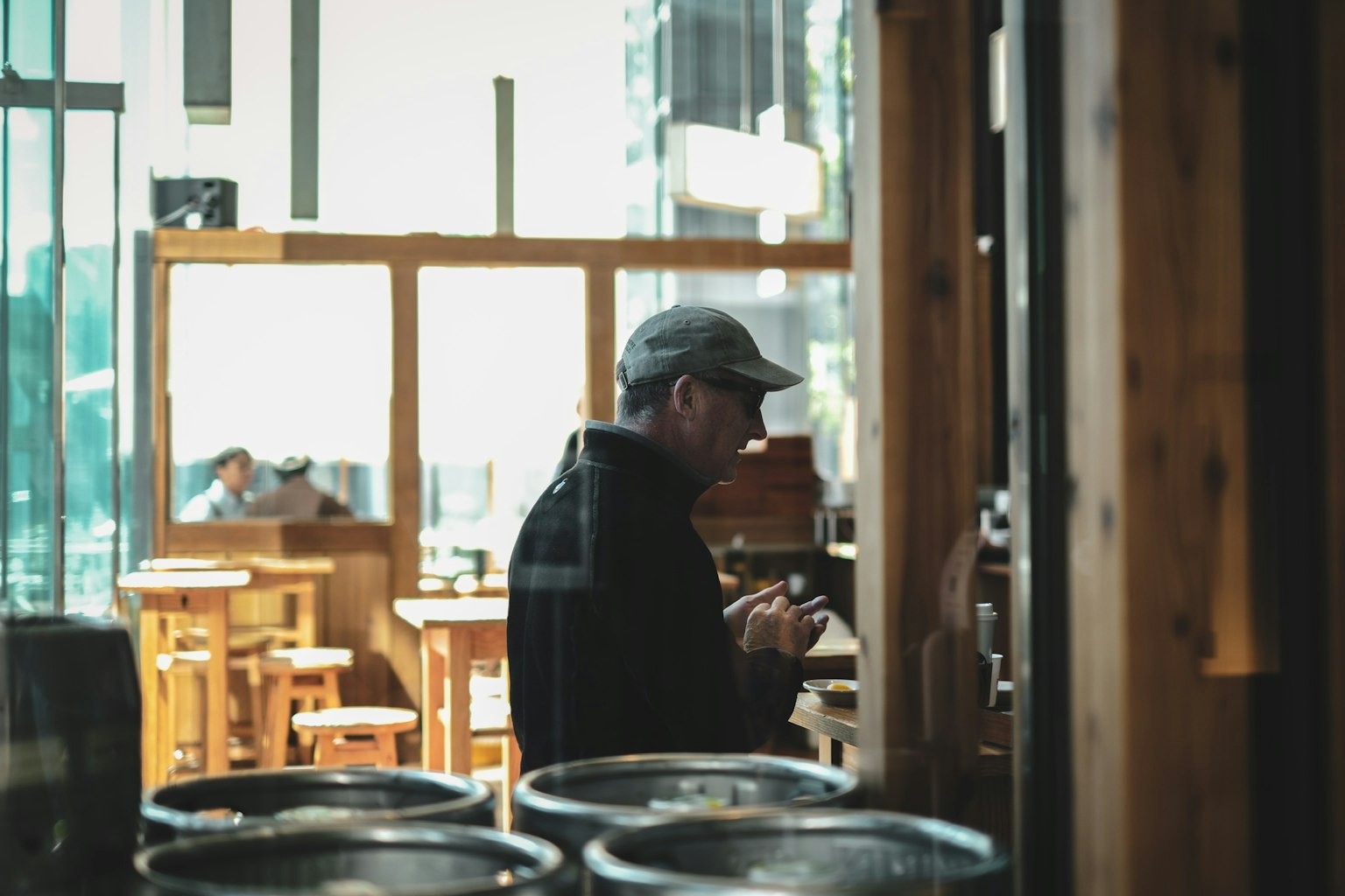 カフェの内部でスマートフォンを操作する男性のシルエット 木製のテーブルと椅子が見える