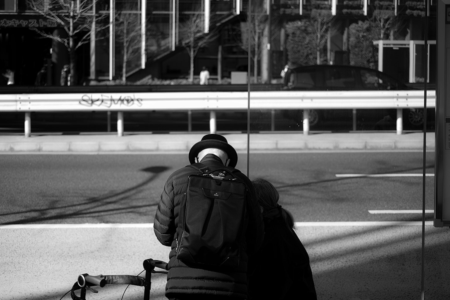 Un paisaje urbano en blanco y negro con una persona con una mochila reflejada en el vidrio