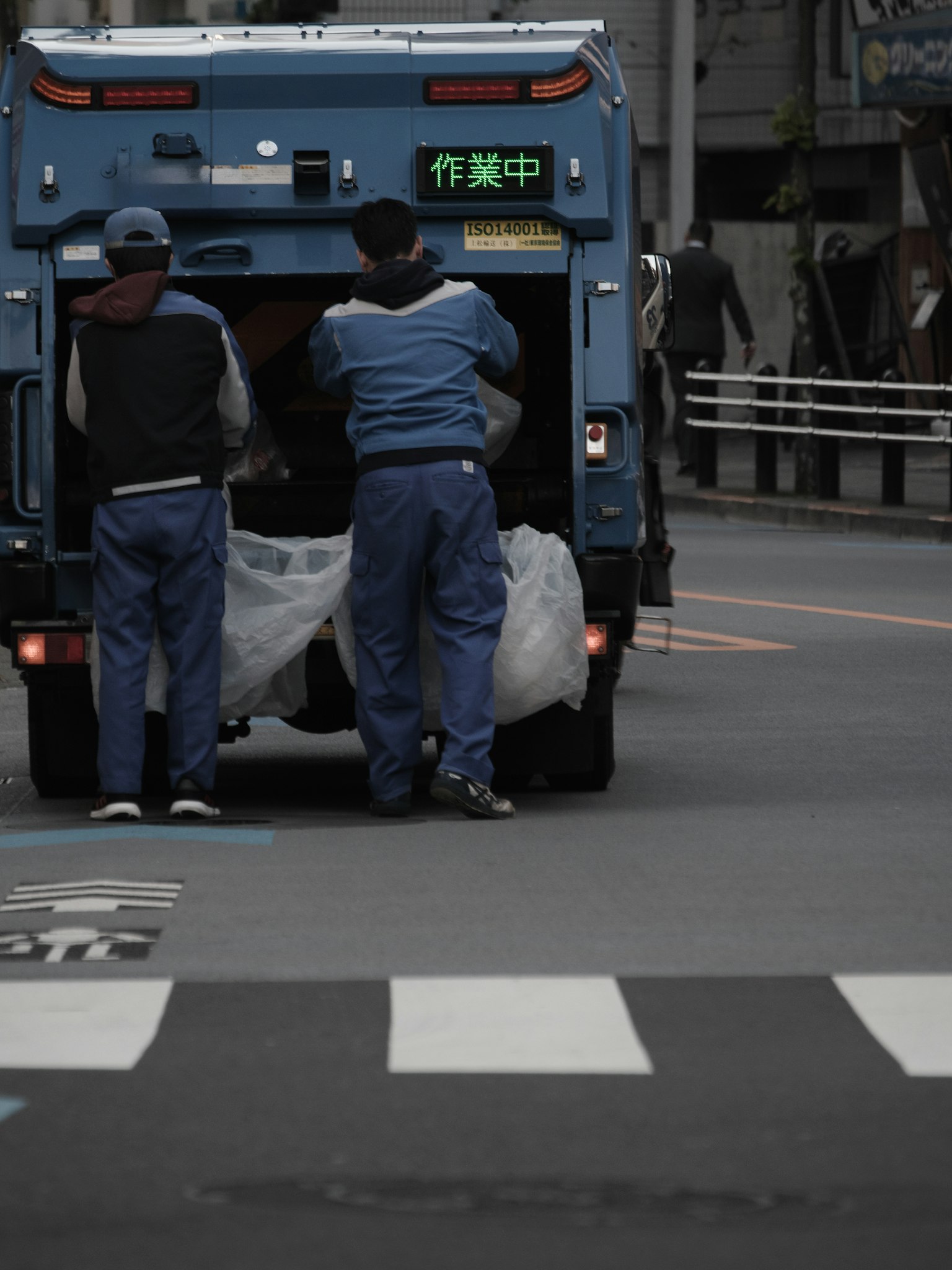 Two workers operating at the back of a blue garbage truck