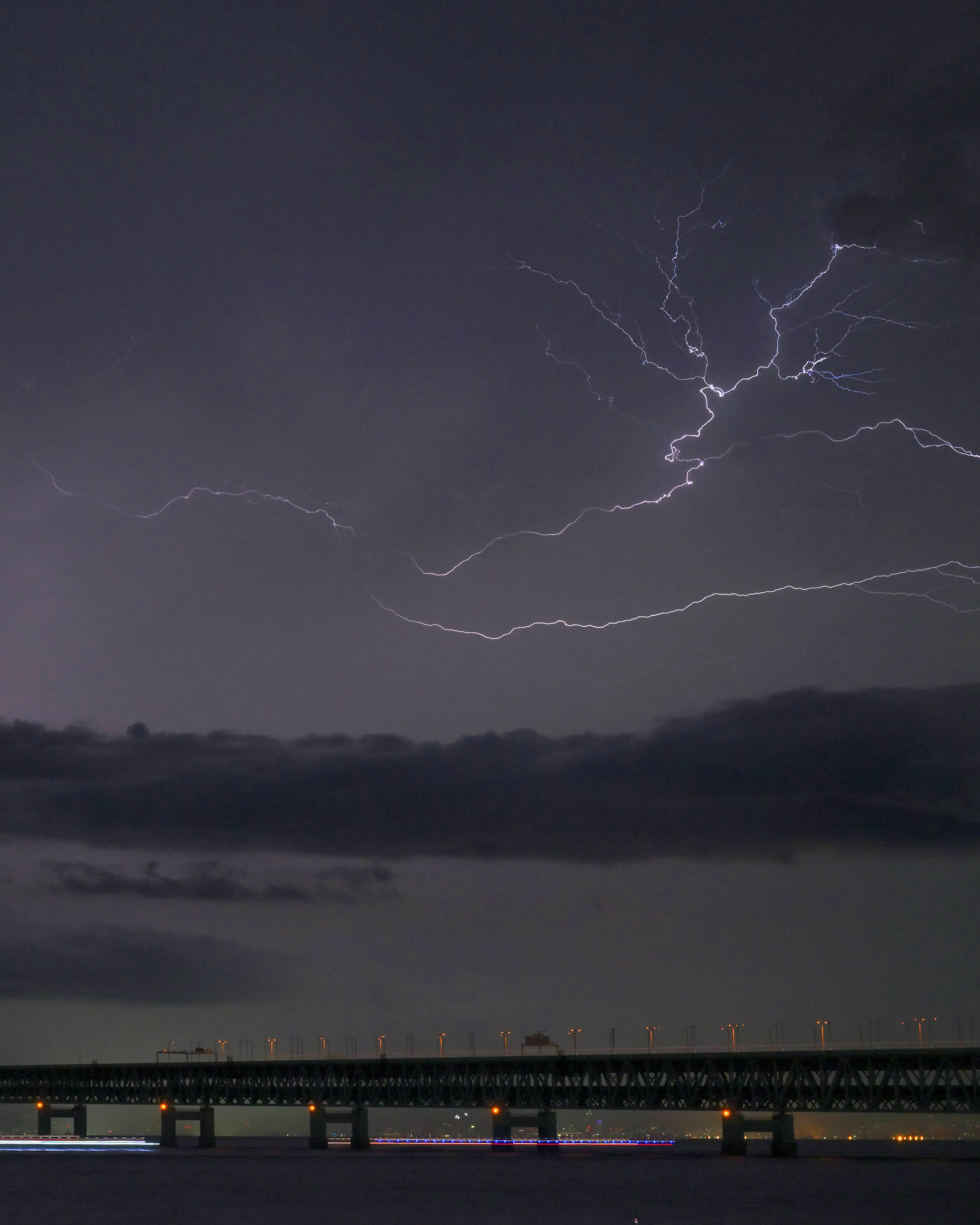 雷雲の下で光る橋と川沿いの夜景