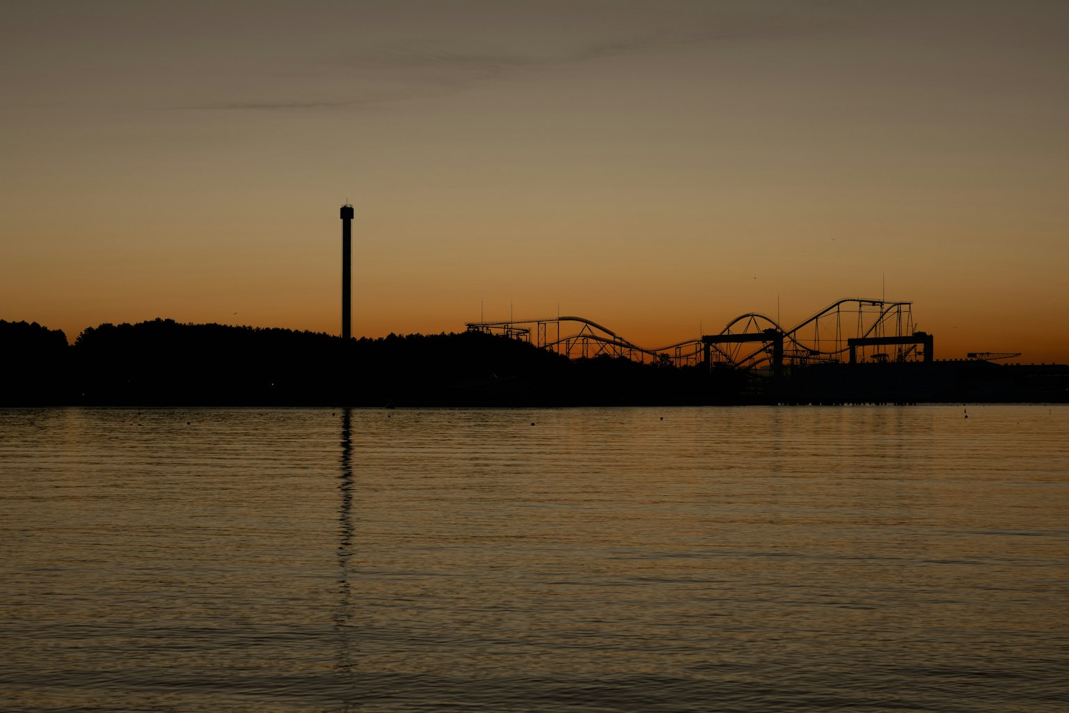 Silhouette d'un parc d'attractions au crépuscule avec reflet sur l'eau