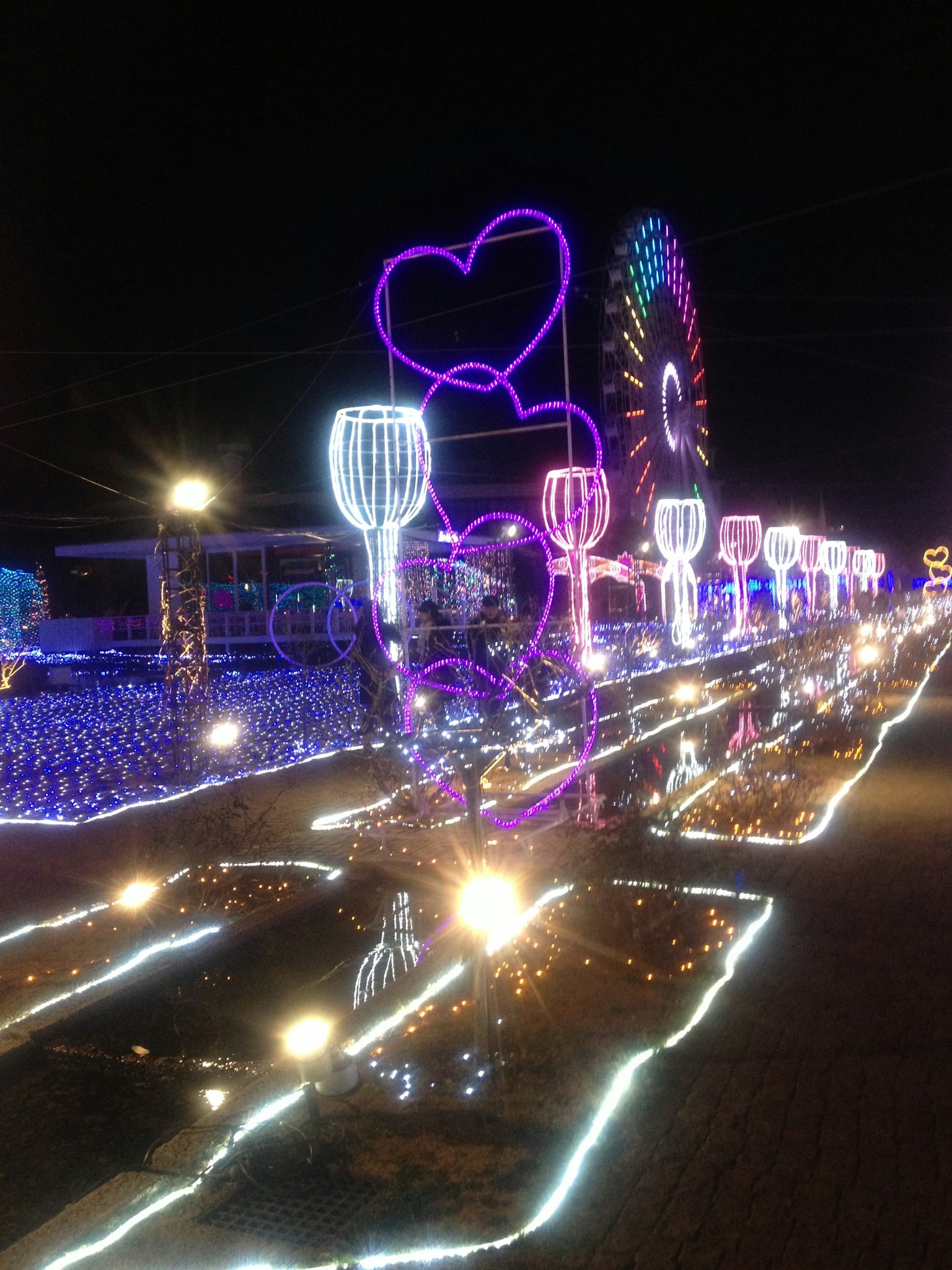 Colorful illuminated decorations and a Ferris wheel in a nighttime festival setting