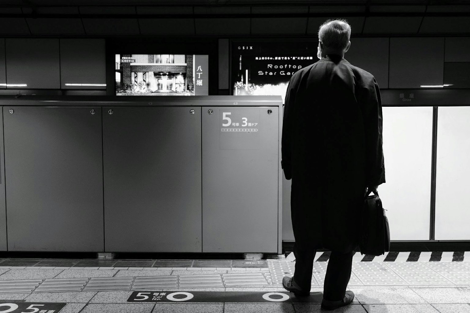 Un homme en manteau noir attendant sur un quai de train