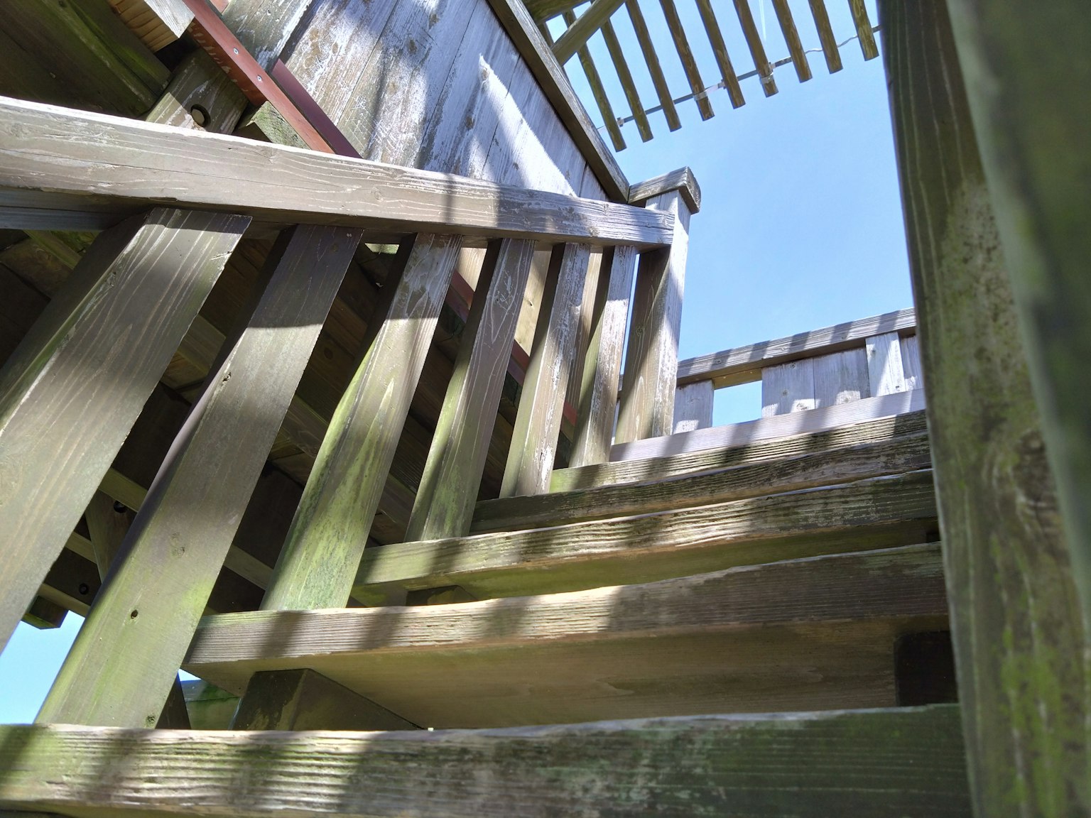 Photo d'escaliers en bois vus d'en bas avec des rampes en bois et un ciel bleu
