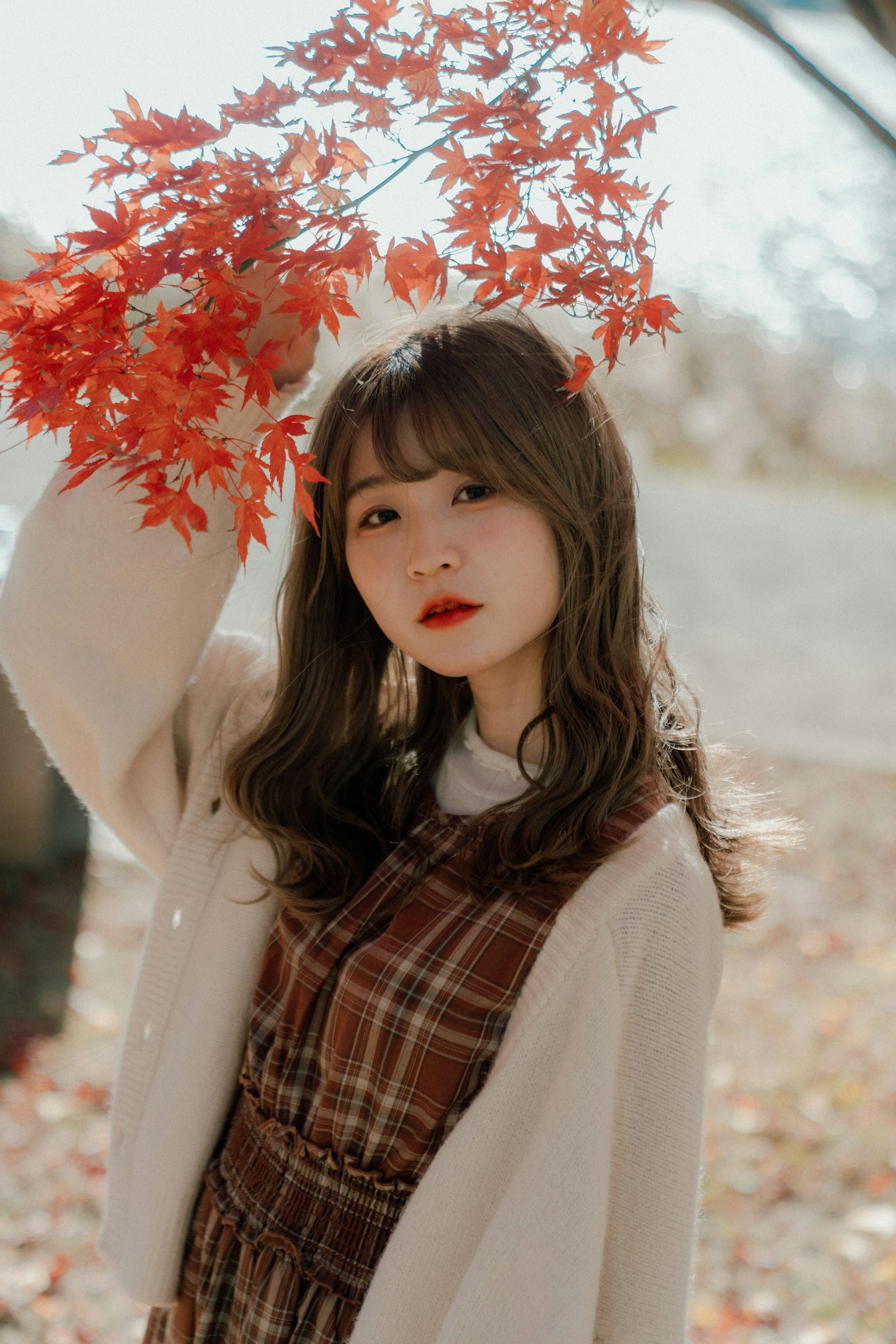 Une femme posant sous des feuilles d'automne tenant un feuillage rouge avec un sourire