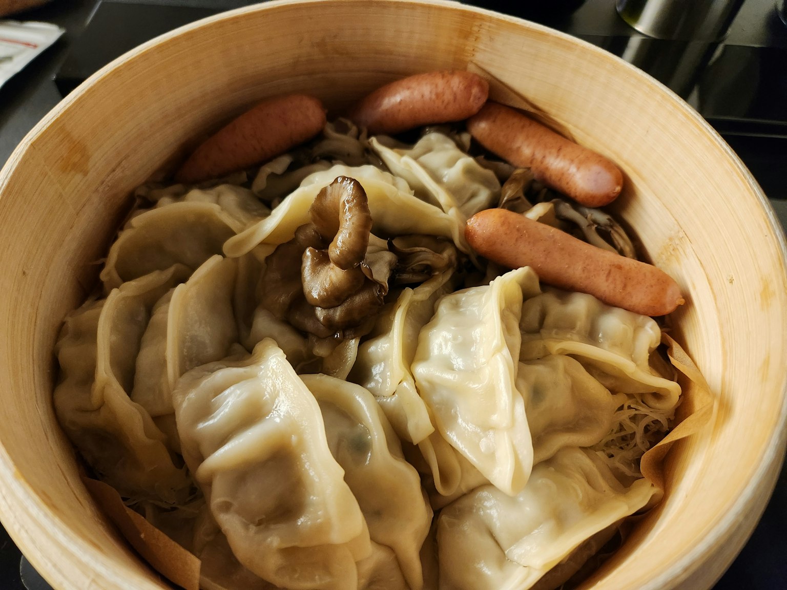Bamboo steamer filled with steamed dumplings and sausages