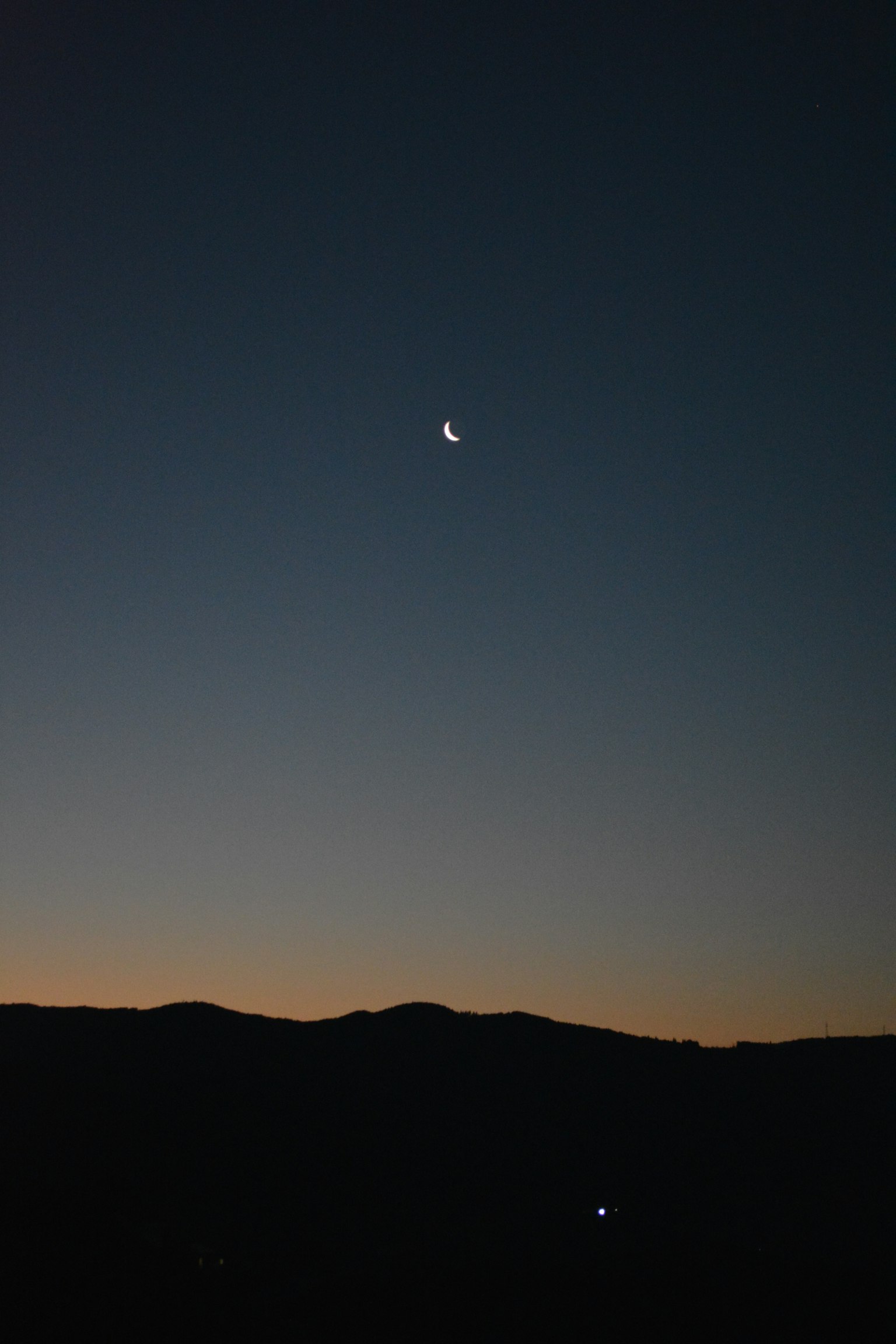 Luna creciente en el cielo nocturno con siluetas de montañas