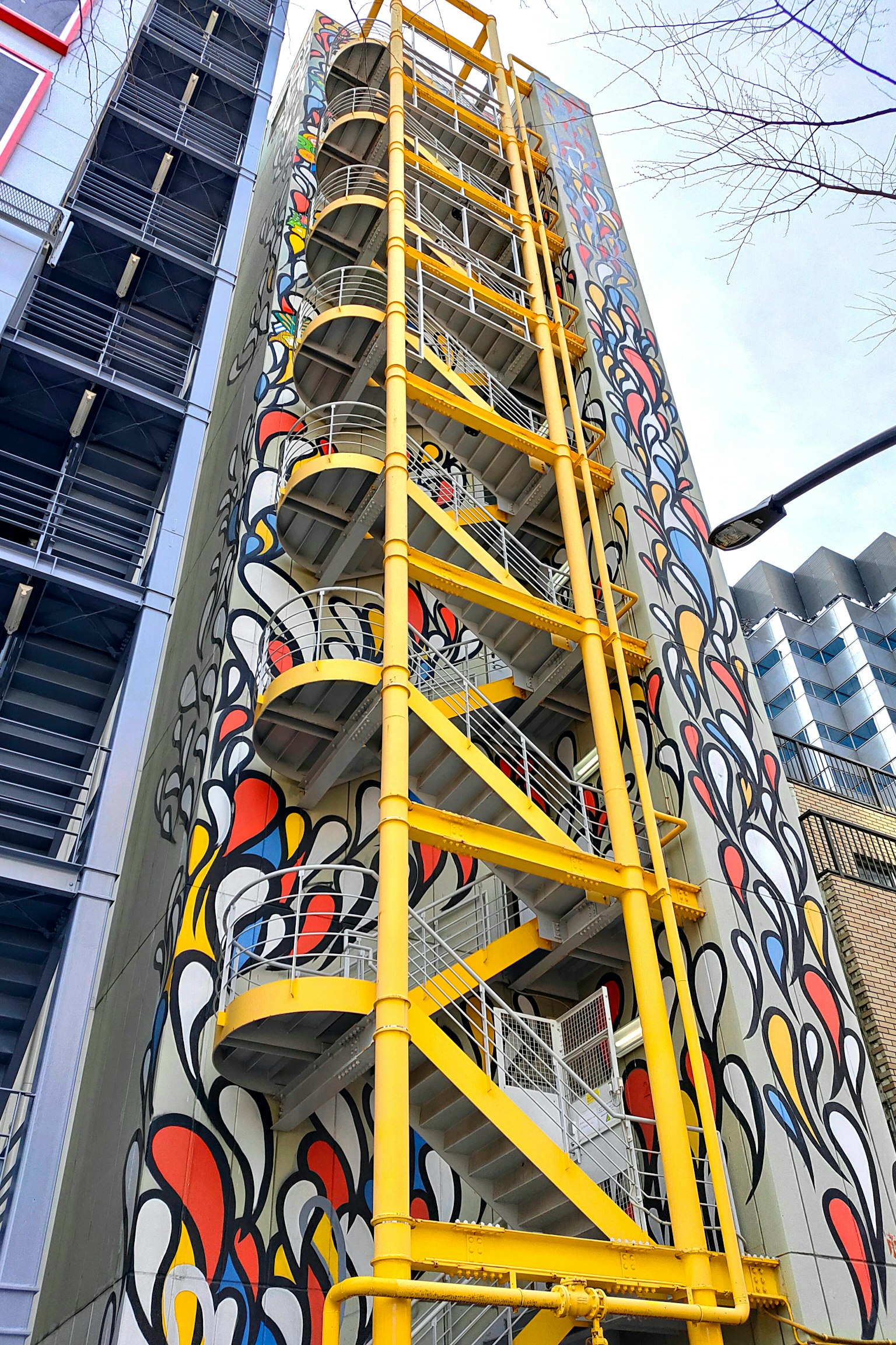 Exterior de un edificio con una escalera en espiral amarilla y un mural colorido