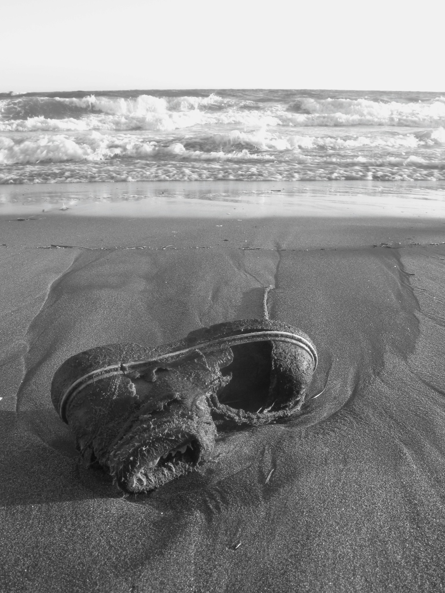 Sepatu tua yang terdampar di pantai dengan ombak lembut
