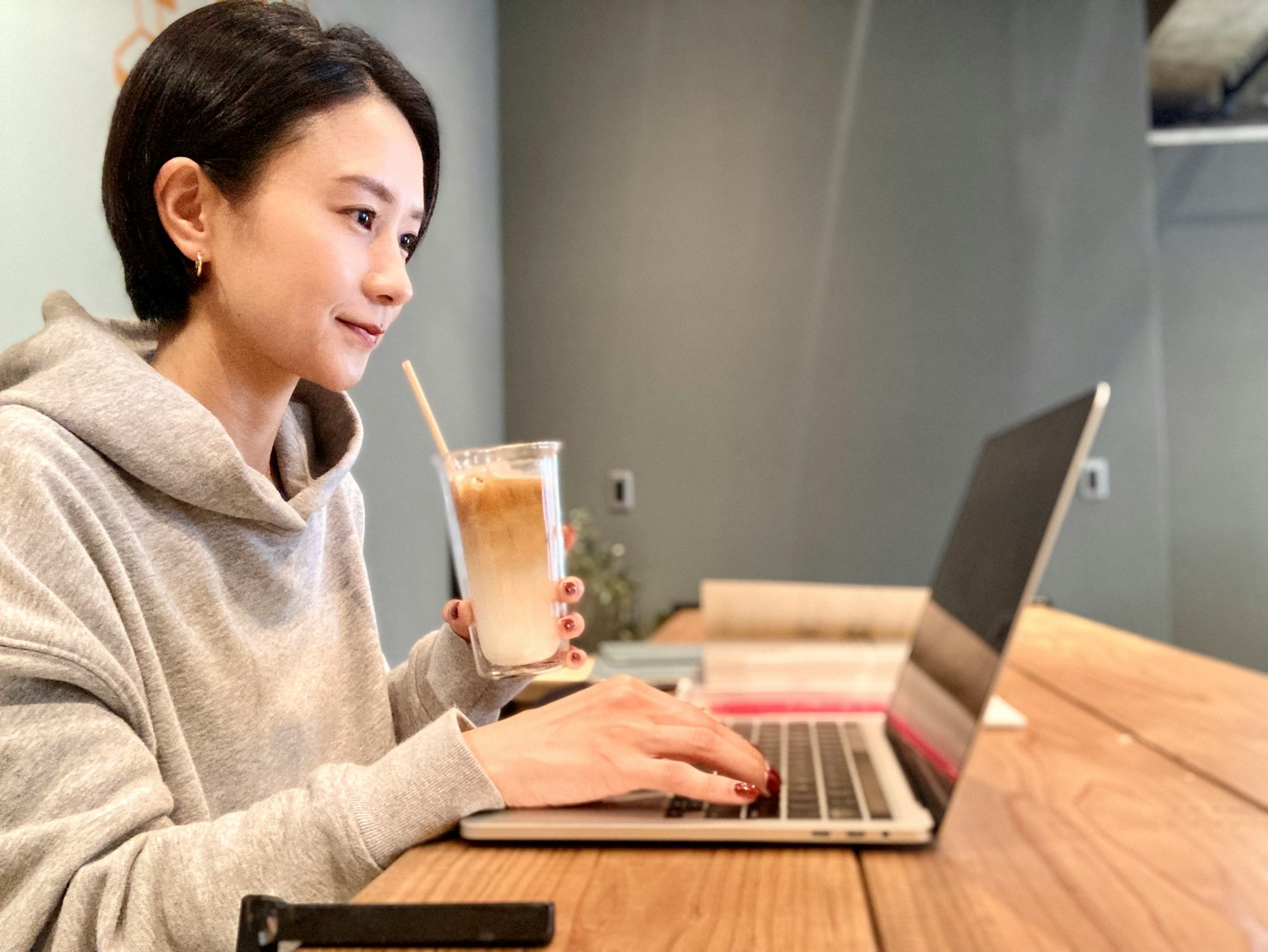 Người phụ nữ làm việc trên laptop trong khi cầm đồ uống ở quán cà phê