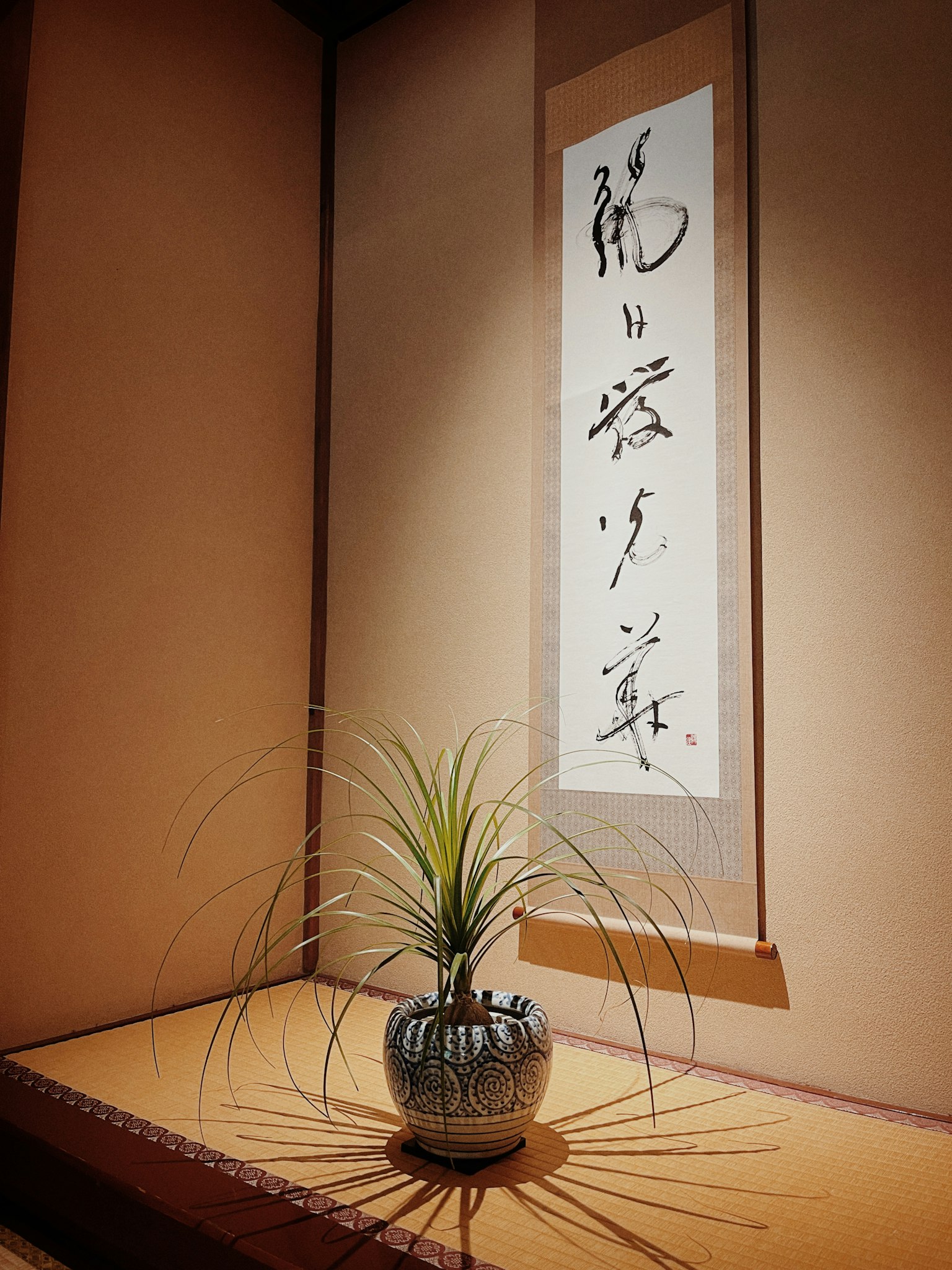 一角落的日本房间，挂着书法卷轴和一个盆栽植物
