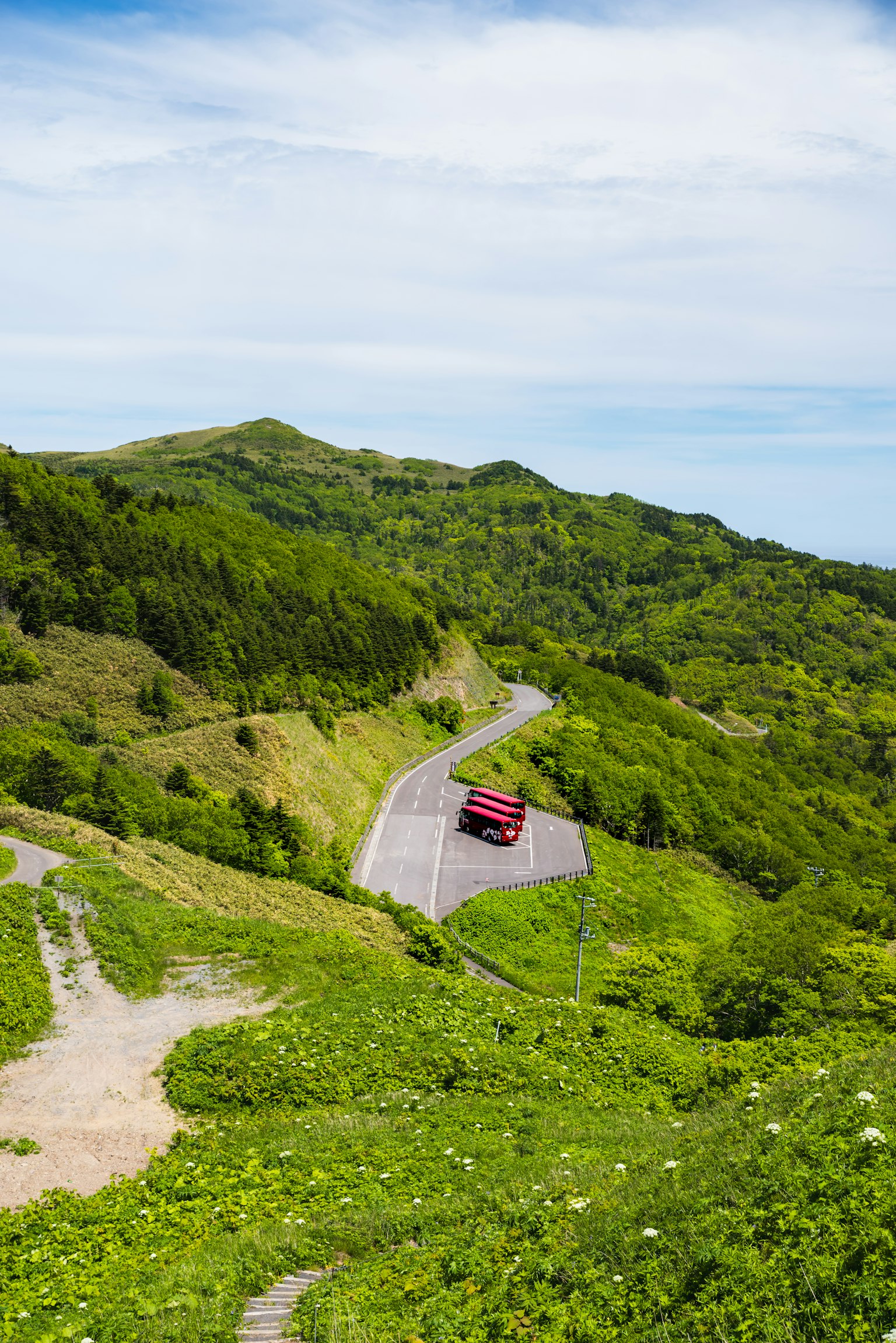 A red car driving along a winding road through lush green hills