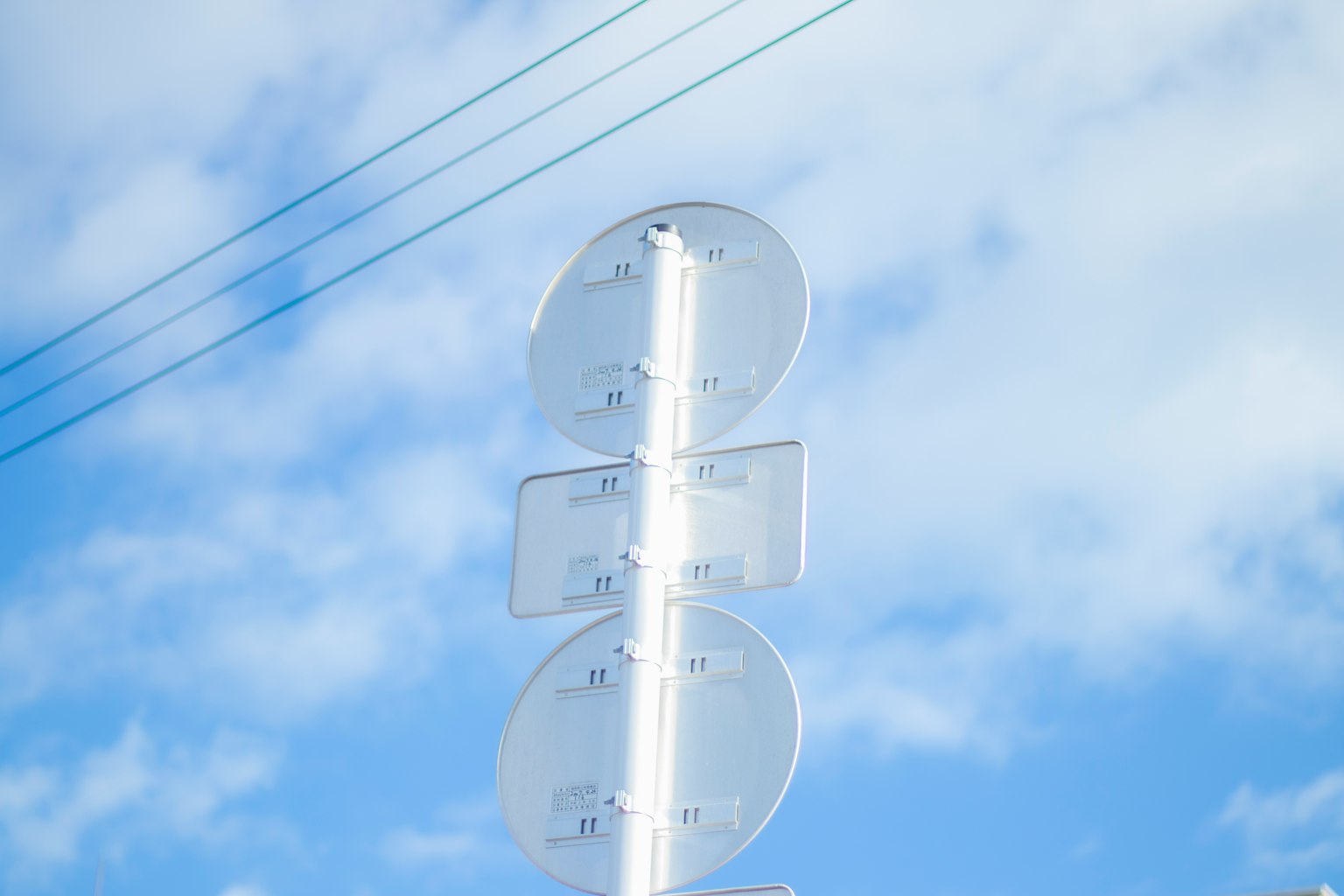 Poste de señal blanca bajo un cielo azul con nubes y cables aéreos