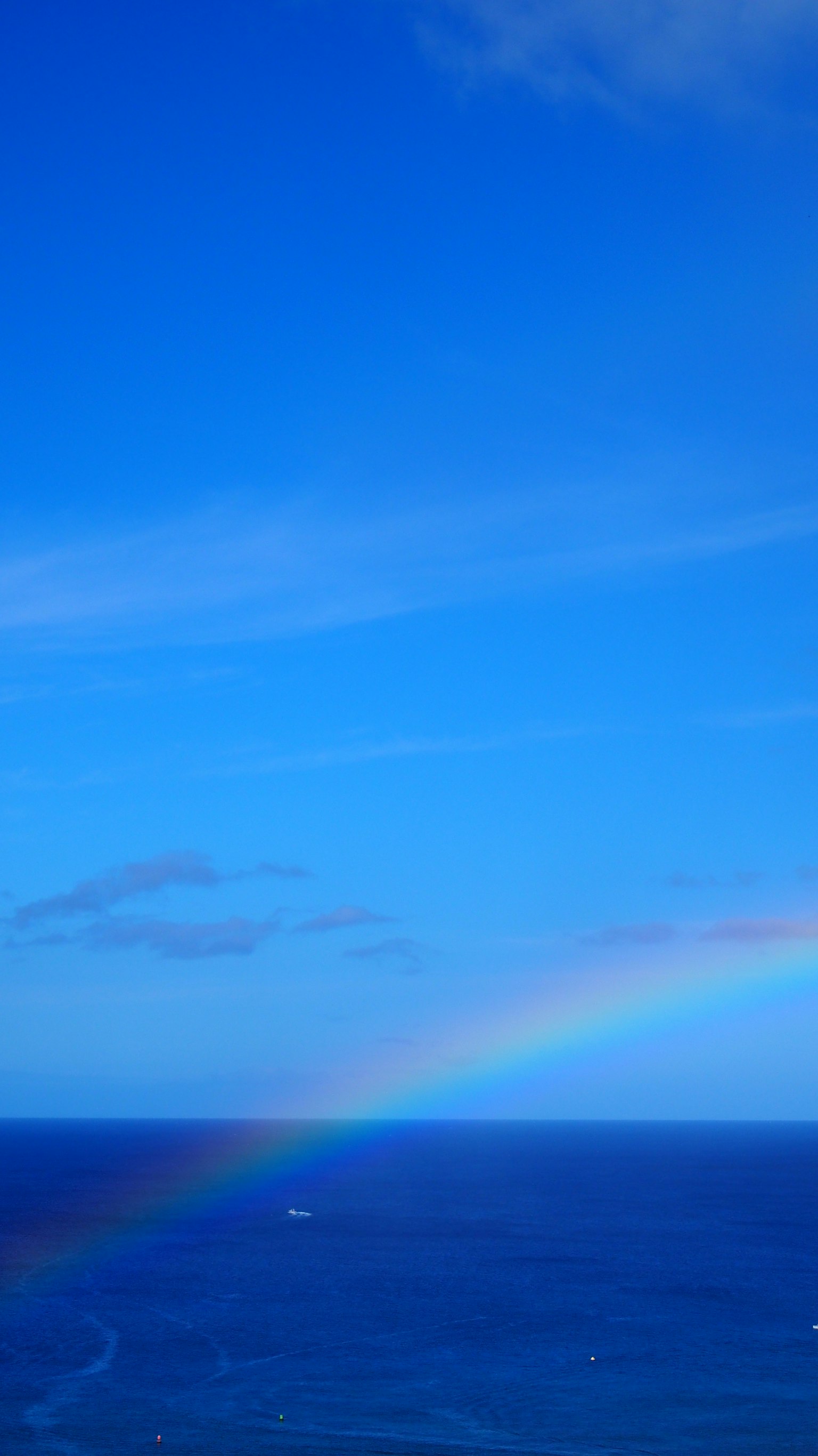 Rainbow arching over a blue ocean under a clear sky