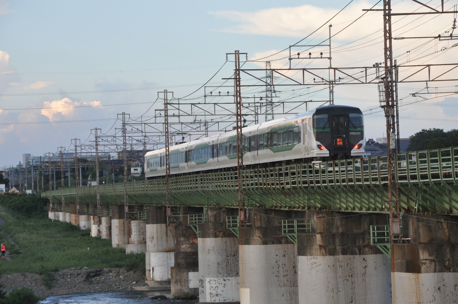 รถไฟที่วิ่งอยู่บนสะพานเขียวเหนือแม่น้ำพร้อมสายไฟฟ้า
