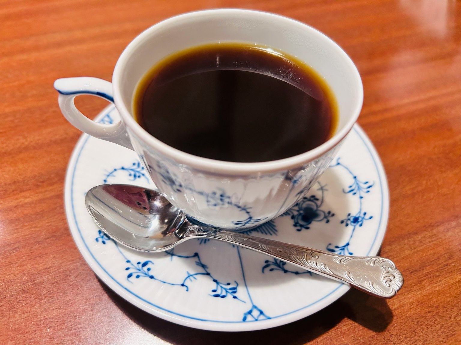 กาแฟดำในถ้วยลายดอกไม้สีน้ำเงินพร้อมช้อน