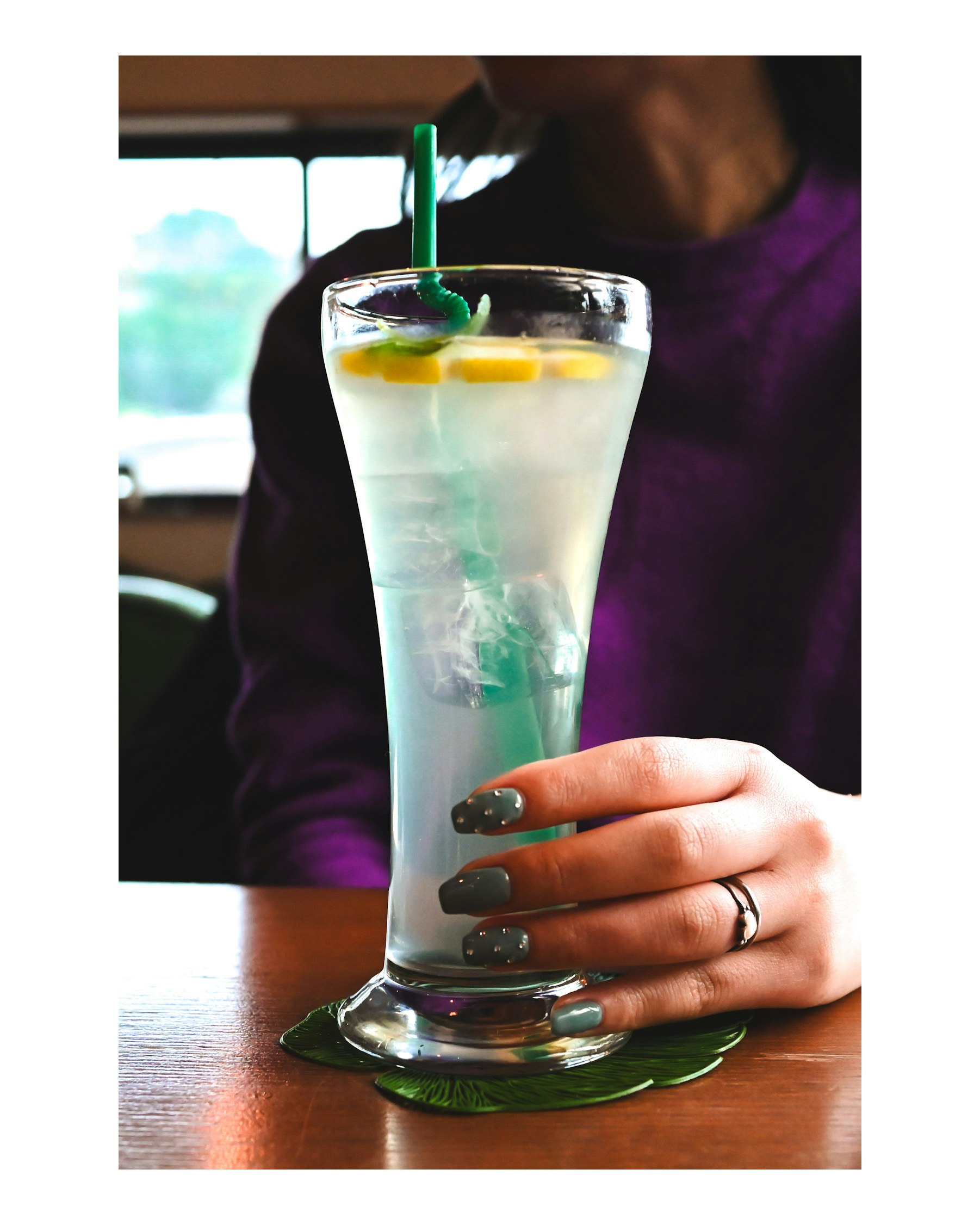 limonada en un vaso alto con menta y pajita sobre una mesa de cafetería