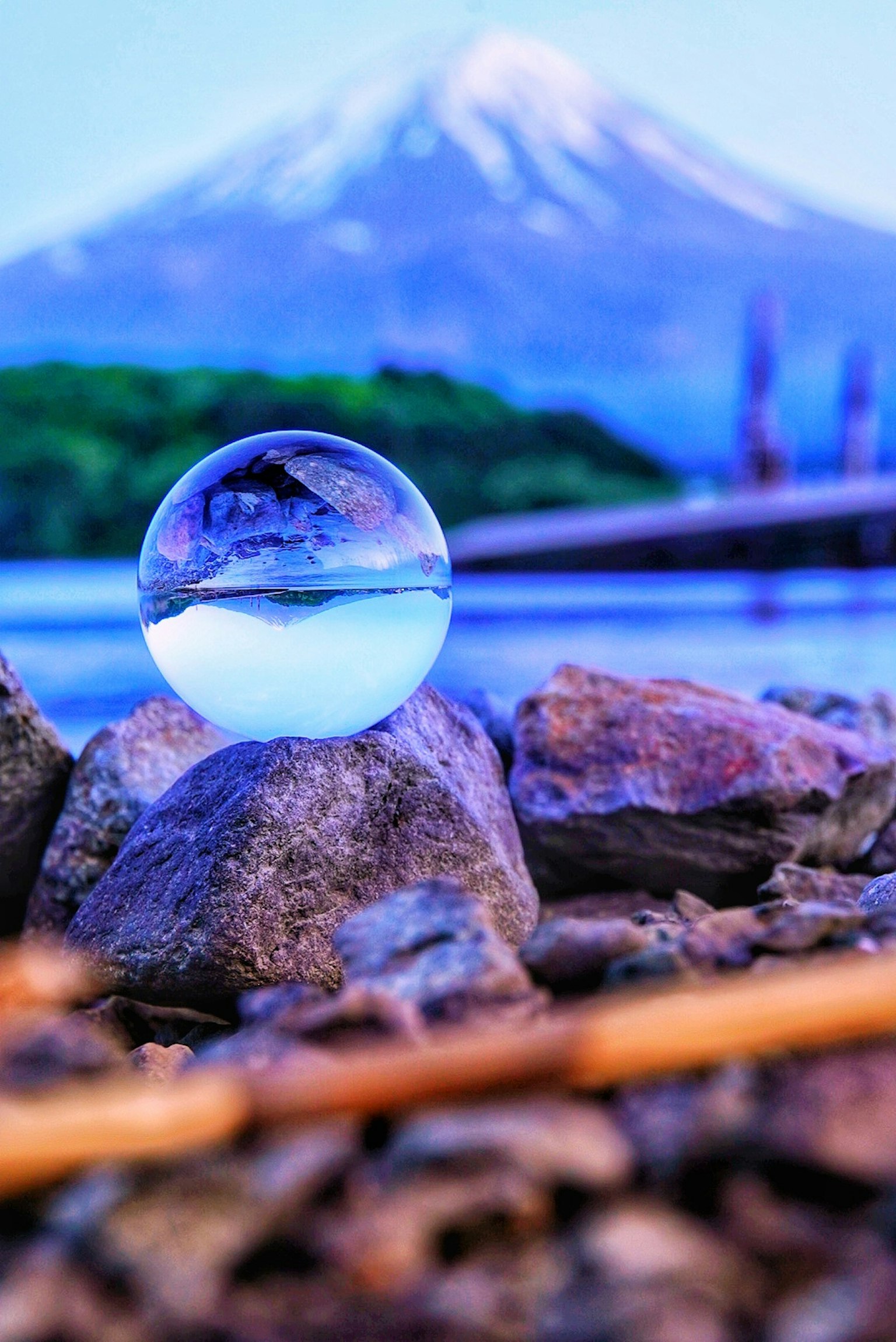Una sfera trasparente che riflette l'acqua si trova su delle rocce con una montagna innevata sullo sfondo
