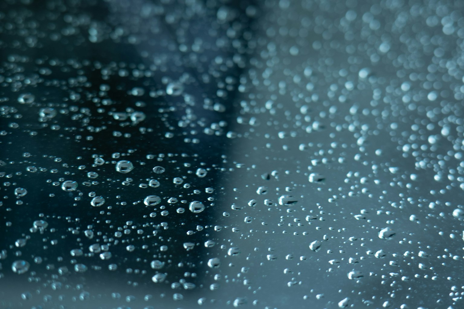 Close-up of water droplets on glass with a bluish green background