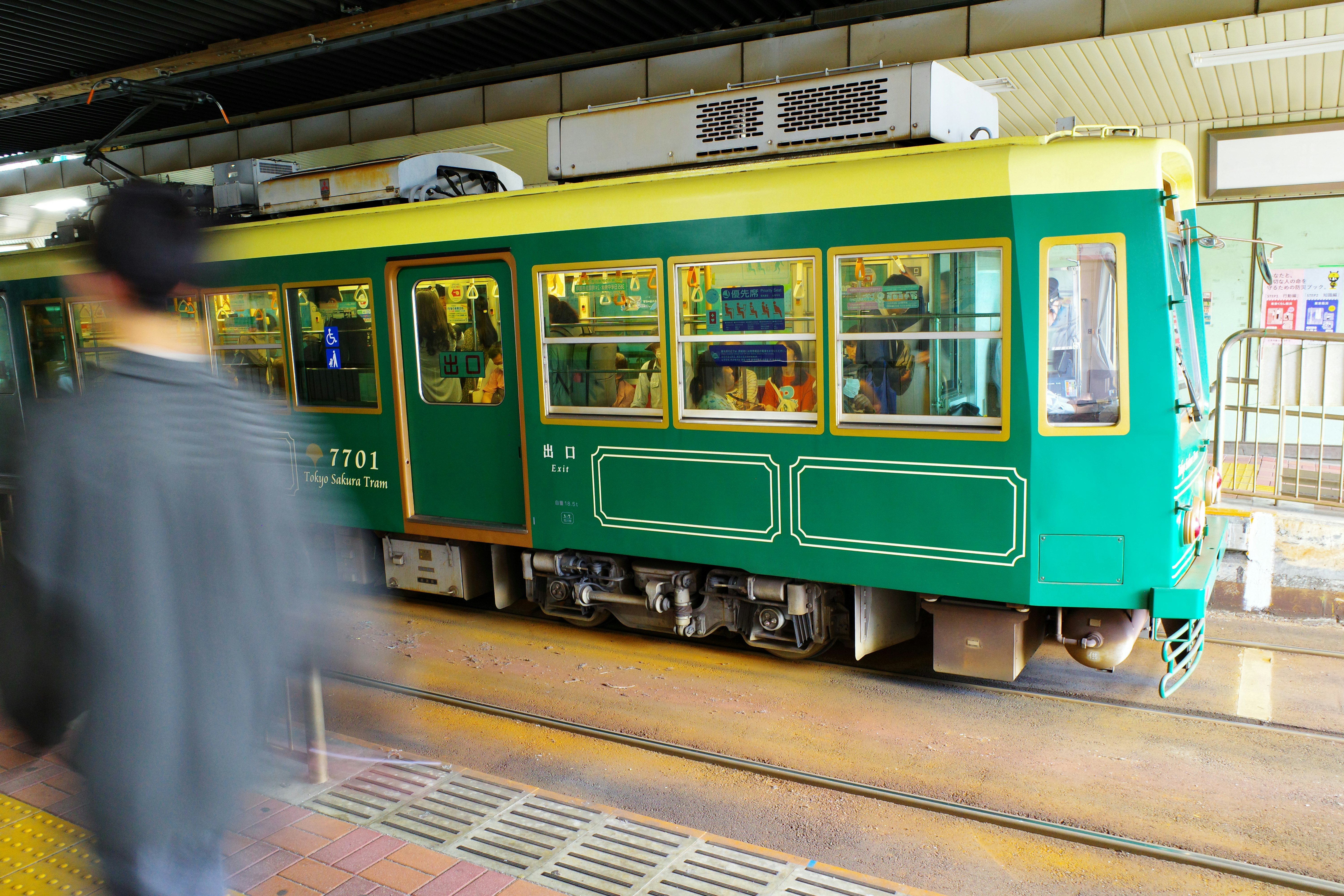 Green streetcar at a station with a blurred pedestrian