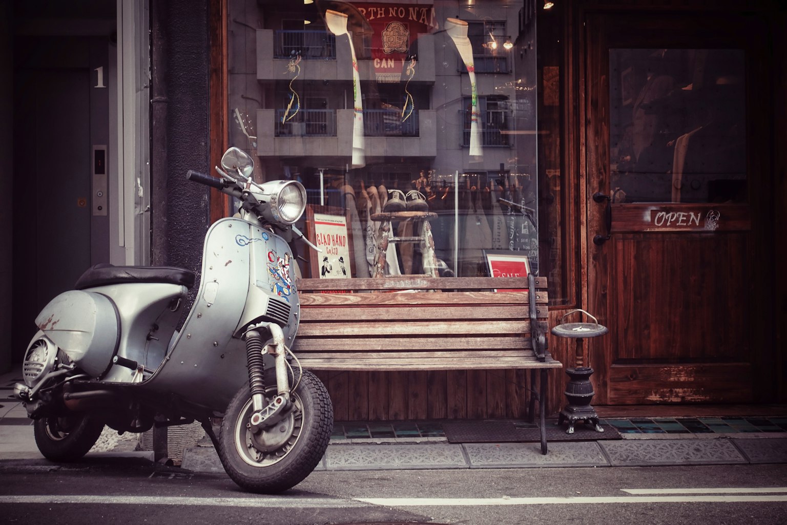 Scooter argento parcheggiato accanto a una panchina di legno davanti a un caffè