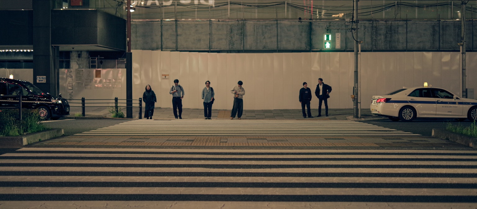 กลุ่มคนยืนอยู่ที่ทางม้าลายในเวลากลางคืนพร้อมแท็กซี่สีขาว