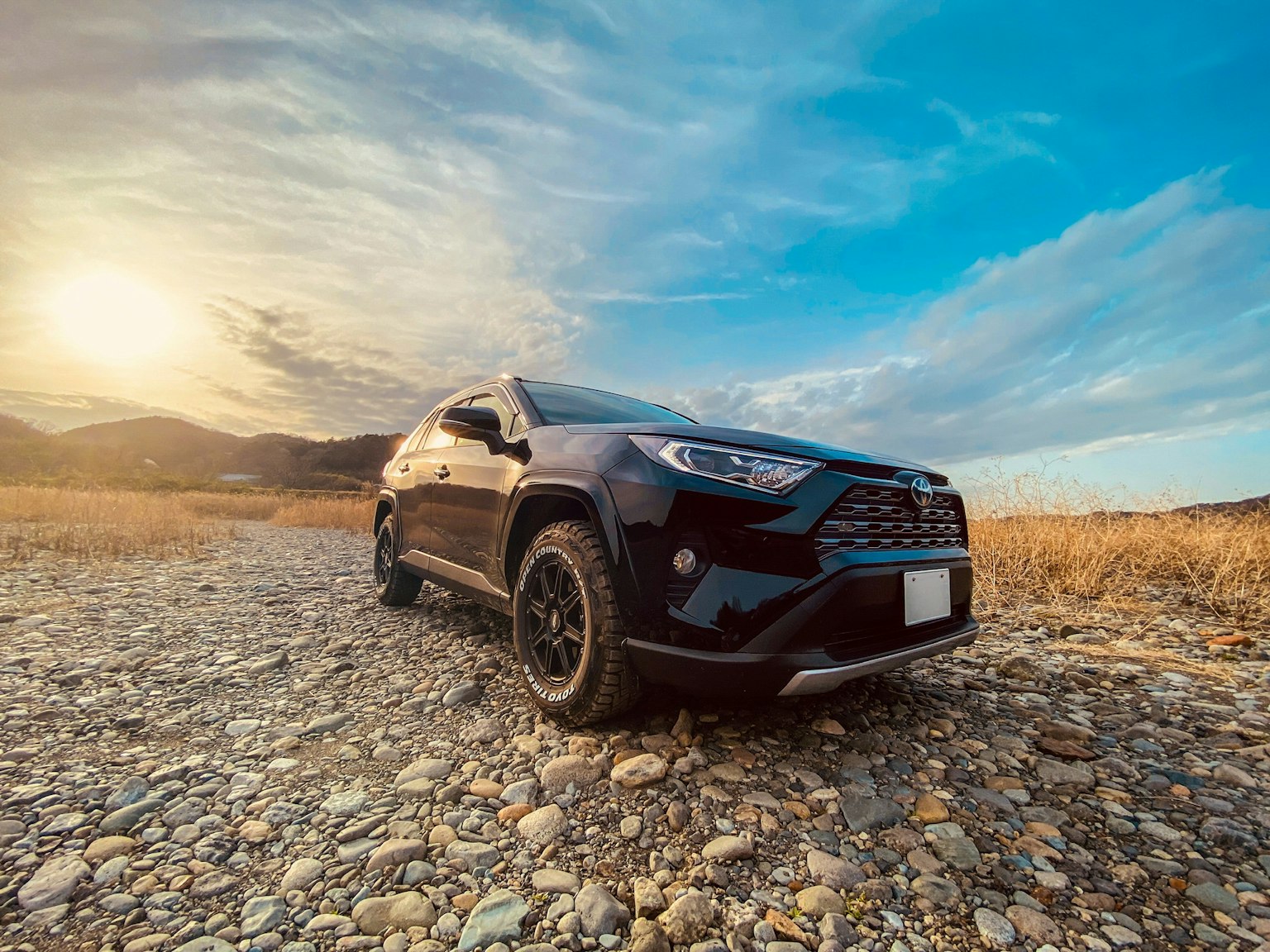 SUV สีดำจอดอยู่บนภูมิประเทศหินมีพระอาทิตย์ตกอยู่เบื้องหลัง