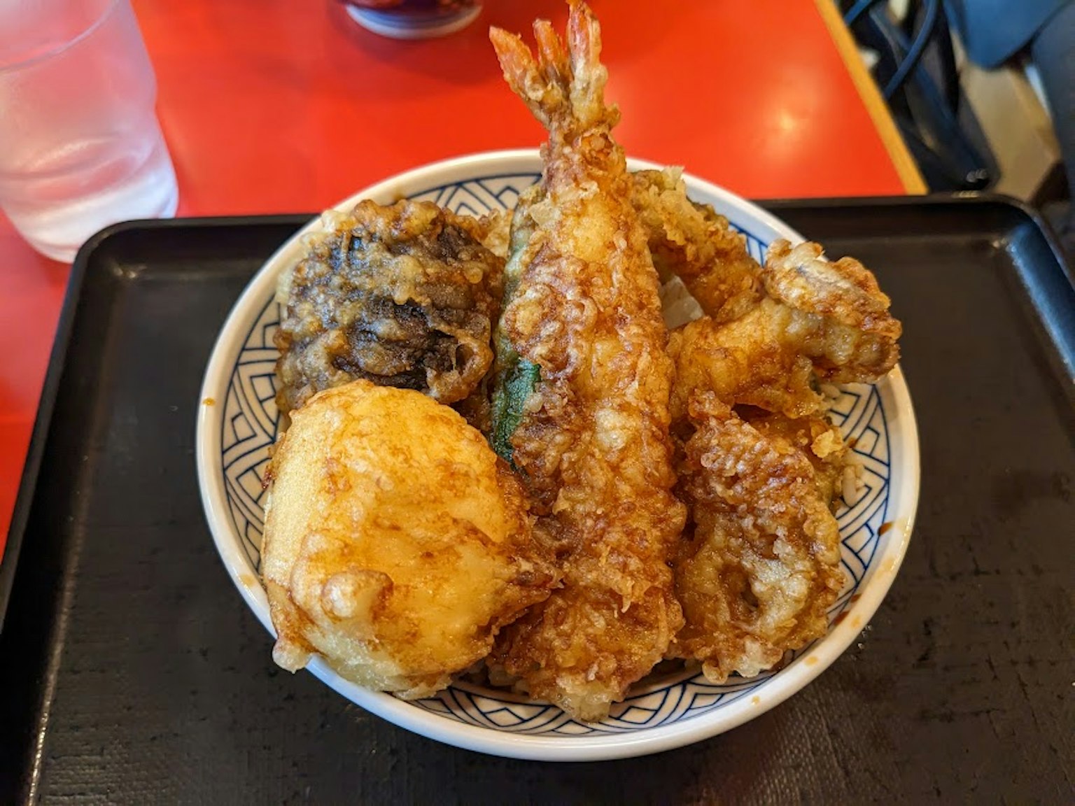 Một bát tempura đa dạng bao gồm tôm và rau trên bàn đỏ