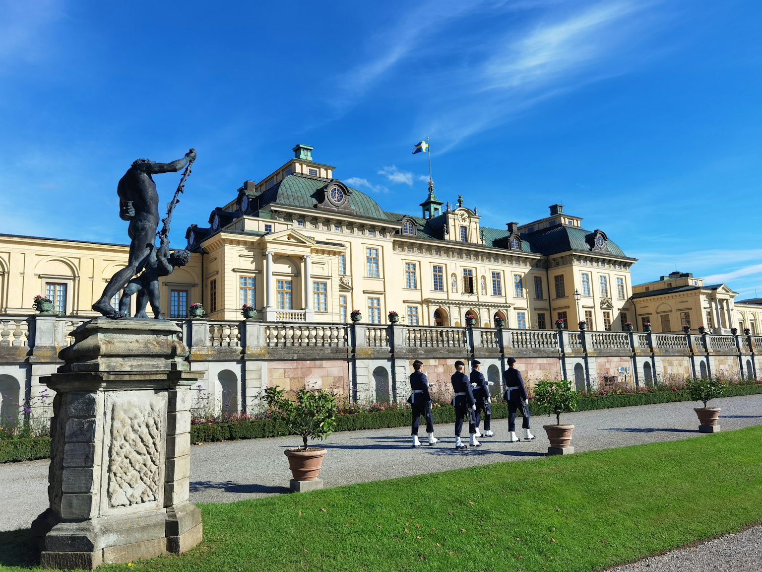 Istana Drottningholm di Stockholm di bawah langit biru cerah dengan patung dan orang-orang di latar depan