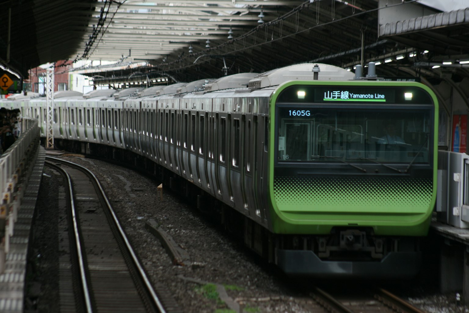 Train vert arrivant à une station avec des voies et un quai