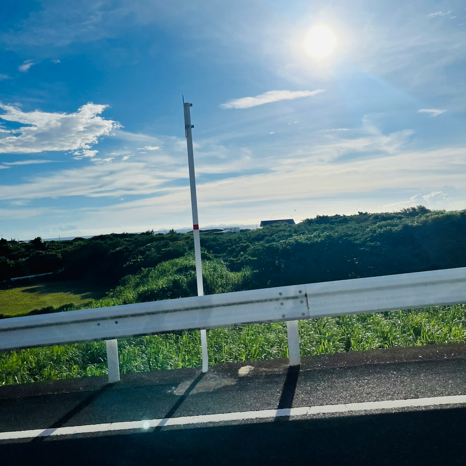 A scenic view with blue sky and white clouds green grassland and a part of the road bright sun shining