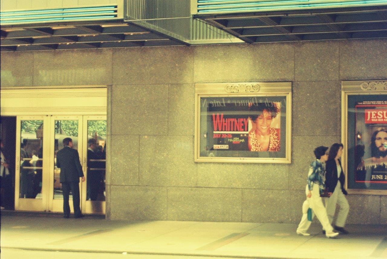 壁面に掲げられたポスターと人が行き交う駅前の通路