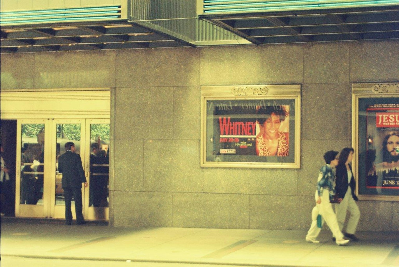 Exterior of a movie theater with people walking by and visible posters
