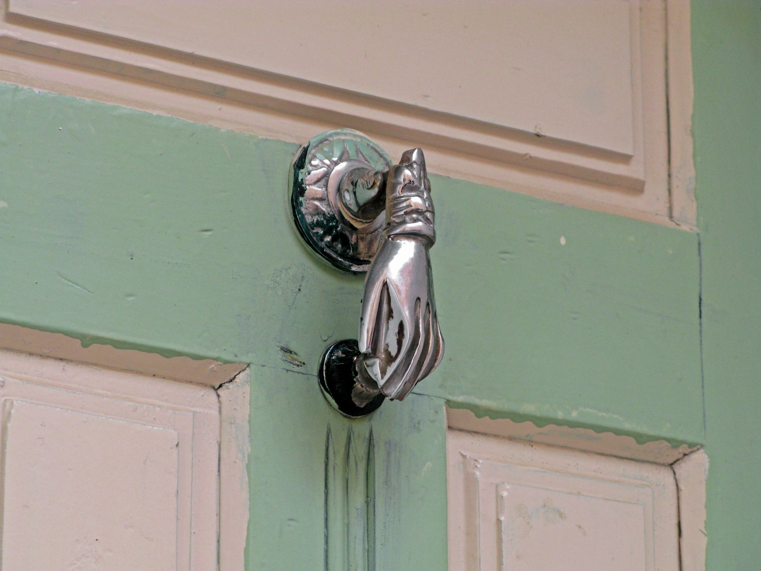 Knocker a forma di mano argentata su una porta verde