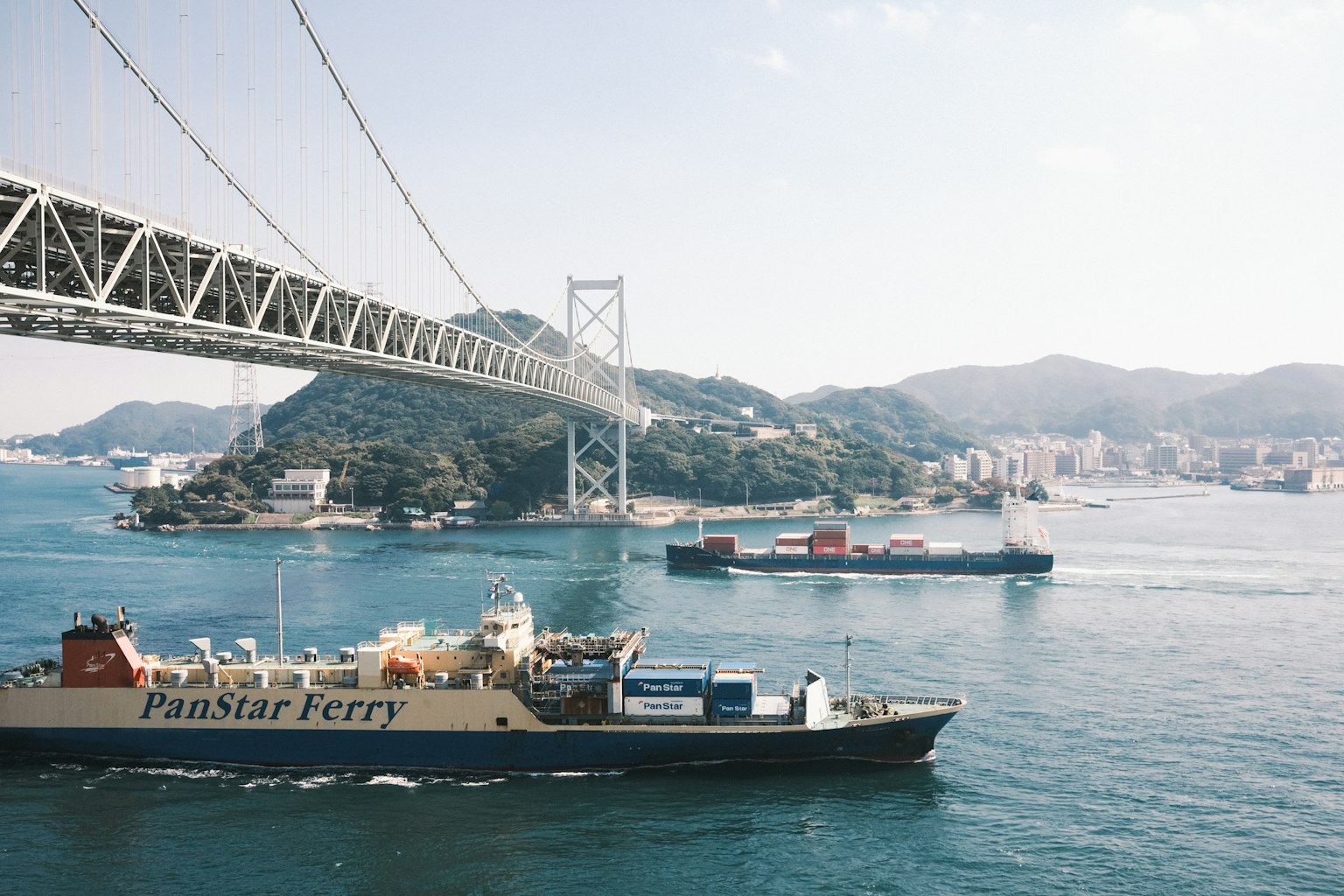 เรือข้ามฟากและเรือบรรทุกสินค้าผ่านใต้สะพานเหนือทะเลสีน้ำเงิน