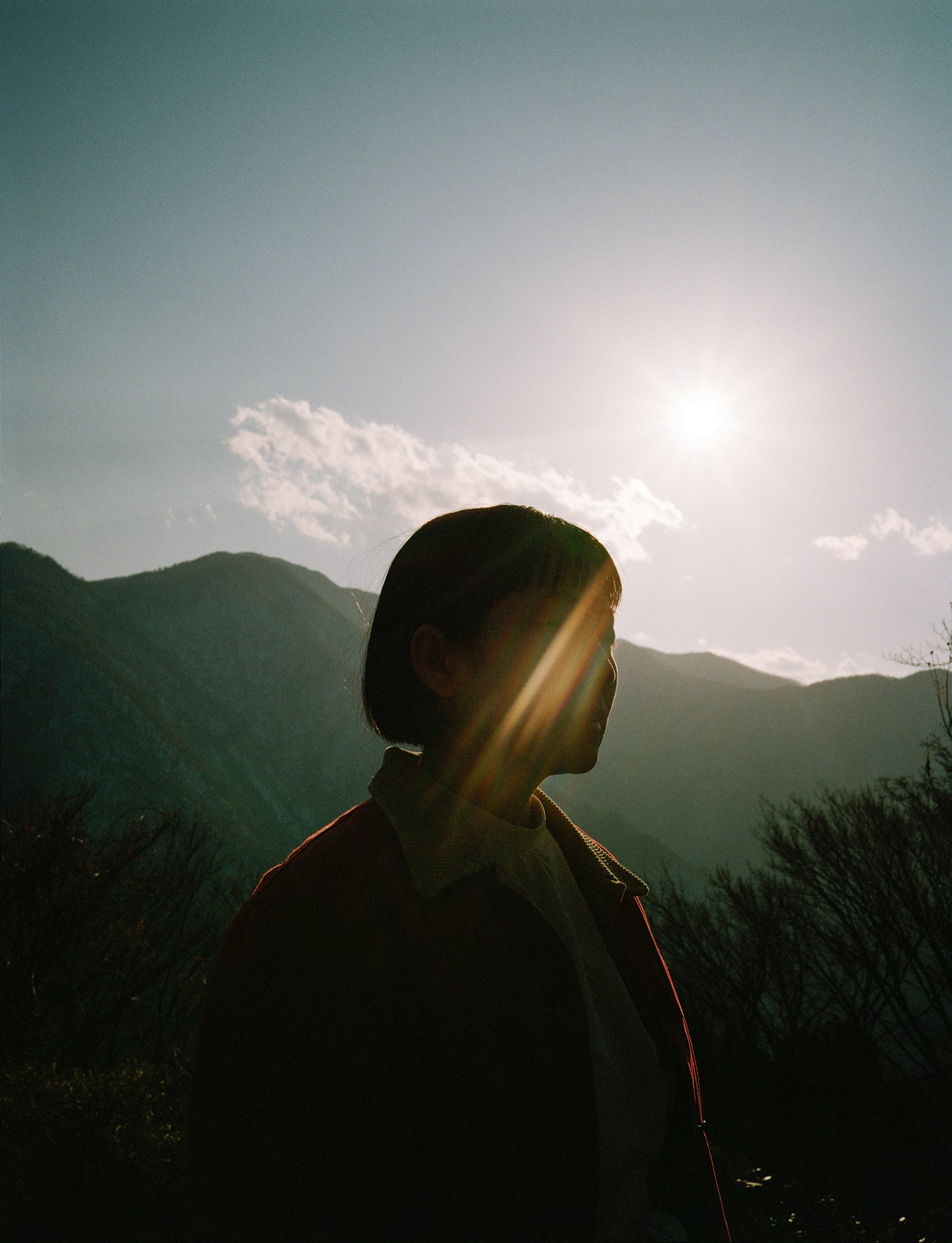 山の背景に立つ女性のシルエットと太陽の光