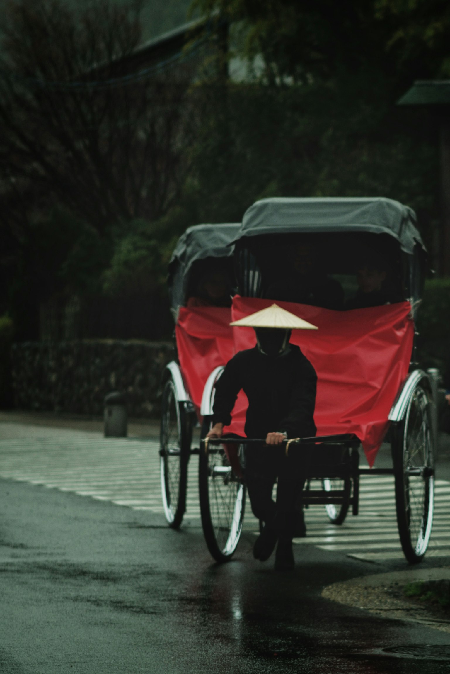 Seseorang berpakaian hitam menarik becak dengan kain merah di tengah hujan