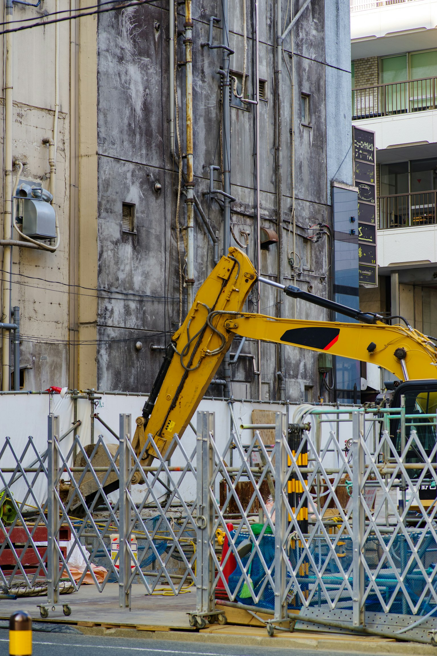 ไซต์ก่อสร้างที่มีรถขุดสีเหลืองและตึกเก่าที่อยู่ด้านหลัง
