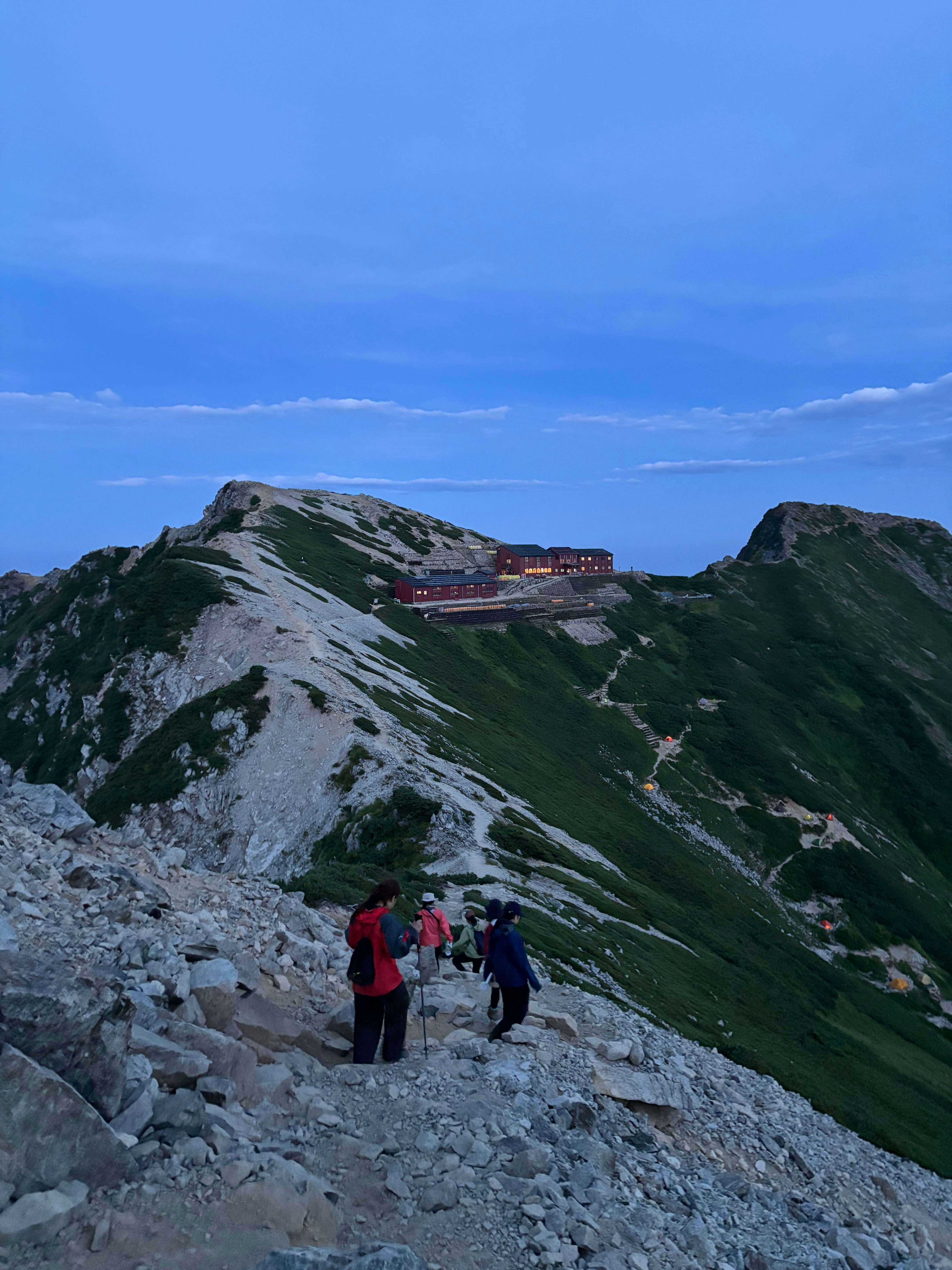稜線の岩場を歩く登山者と山小屋のある山岳風景
