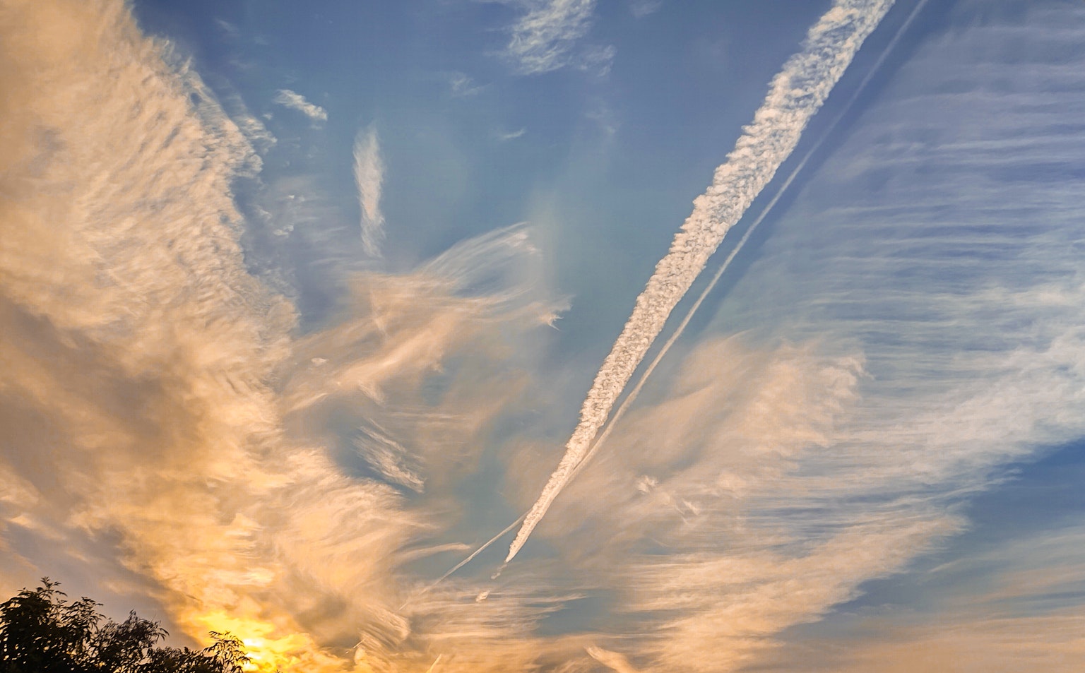 Farbiger Sonnenuntergangshimmel mit zarten Wolken und Kondensstreifen