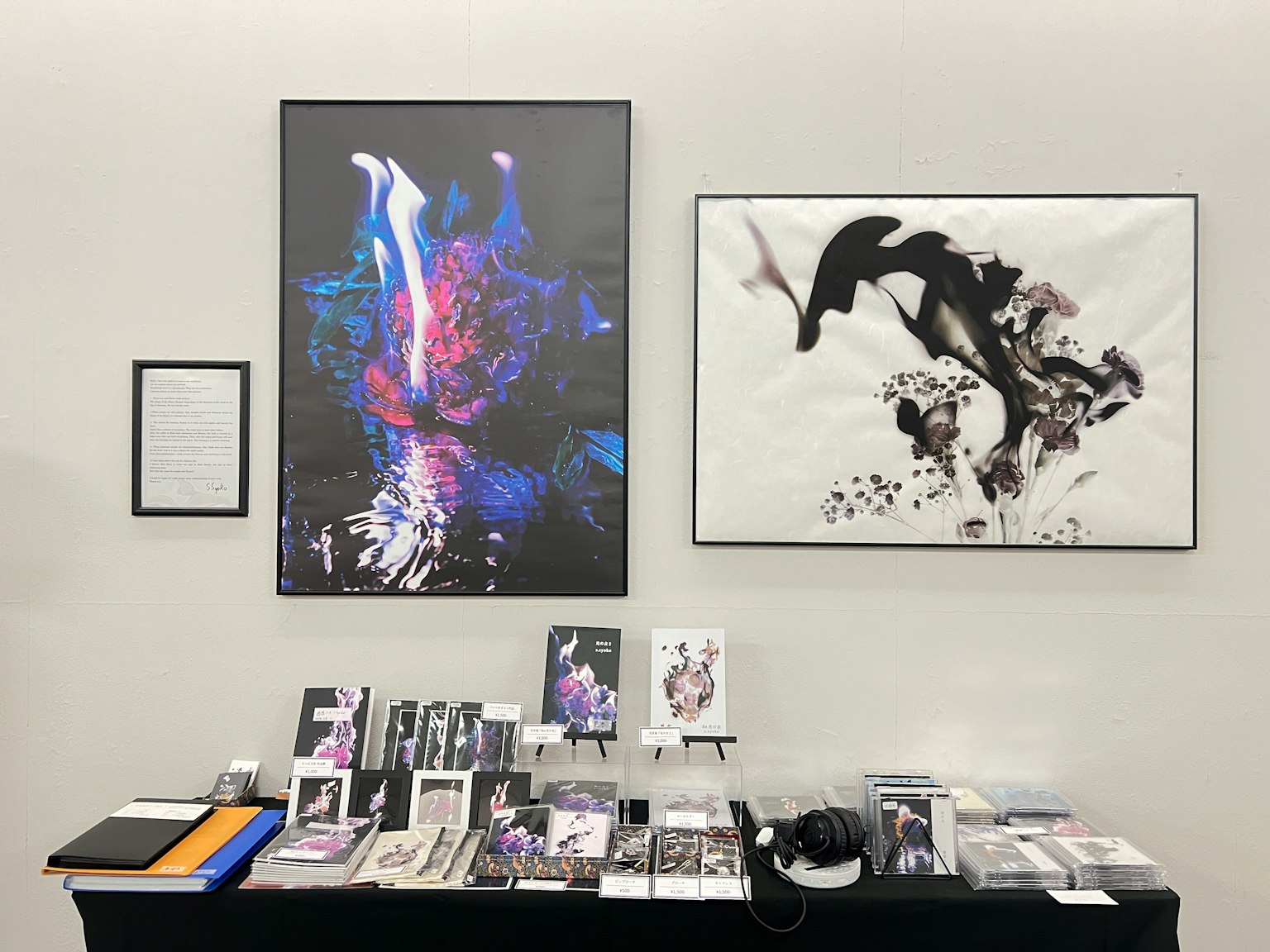 Art exhibition featuring vibrant artwork and monochrome piece displayed on a wall with various items below