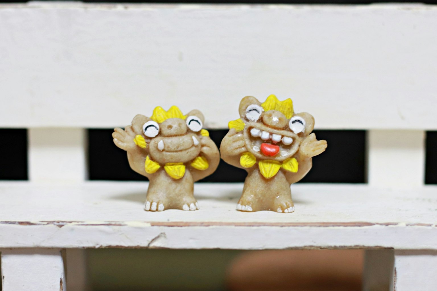 Dos figuritas Shisa adorables con acentos amarillos sobre un fondo blanco