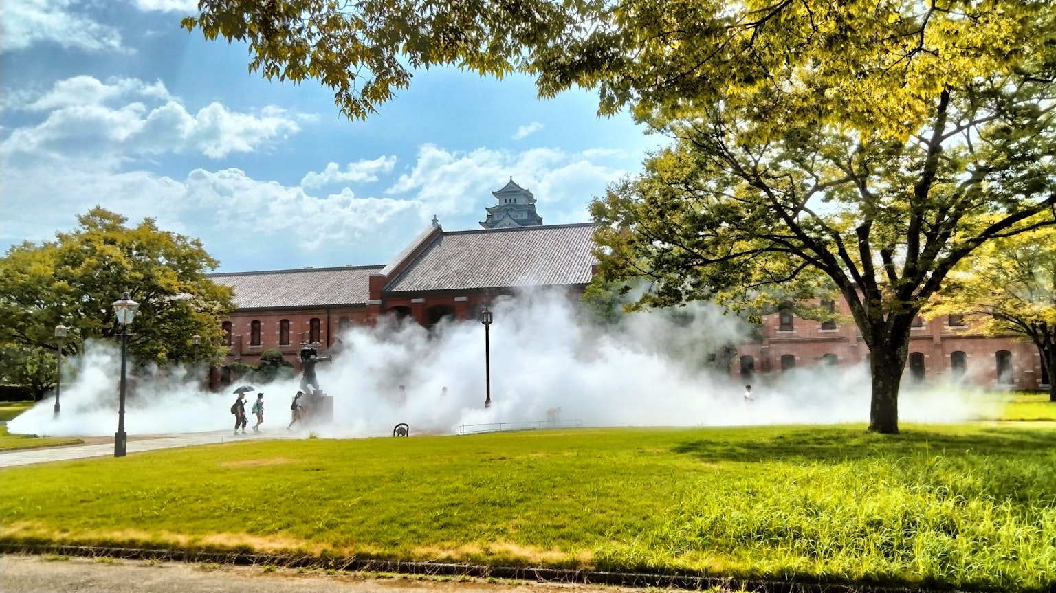 Ein historisches Gebäude umgeben von grünem Gras in einem Park mit aufsteigendem Nebel im Vordergrund