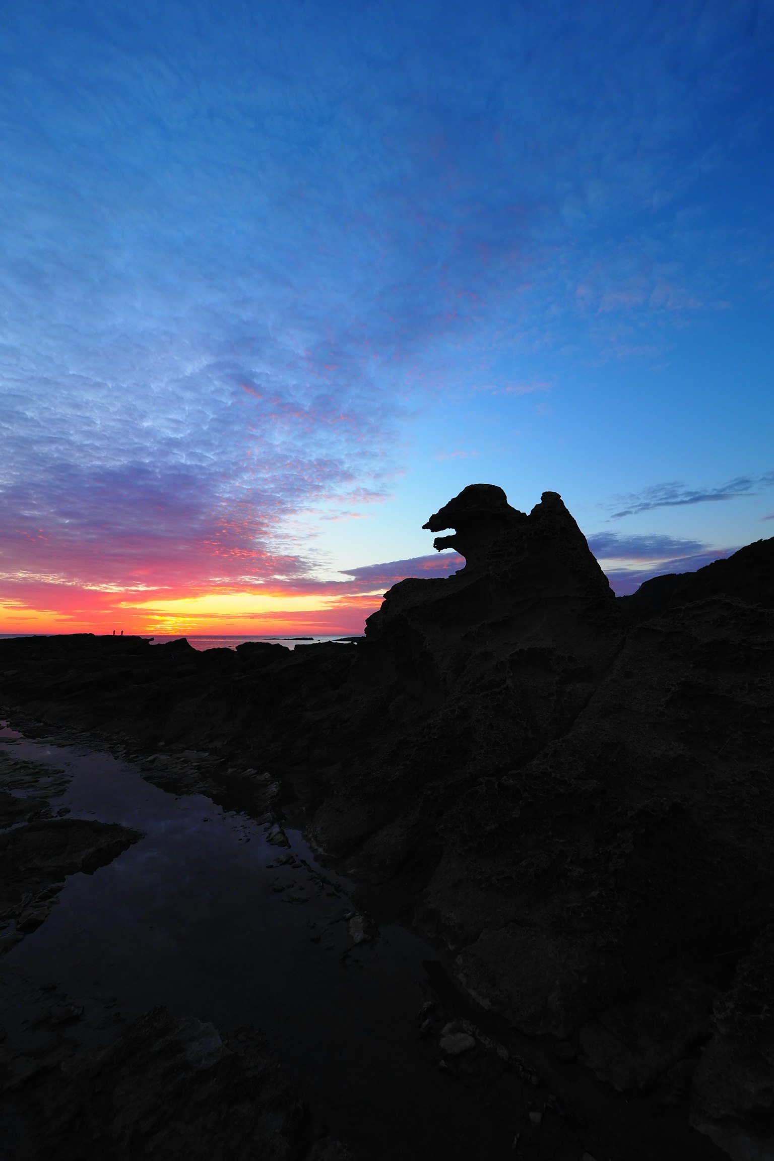 Siluet formasi batu di latar belakang langit senja yang berwarna