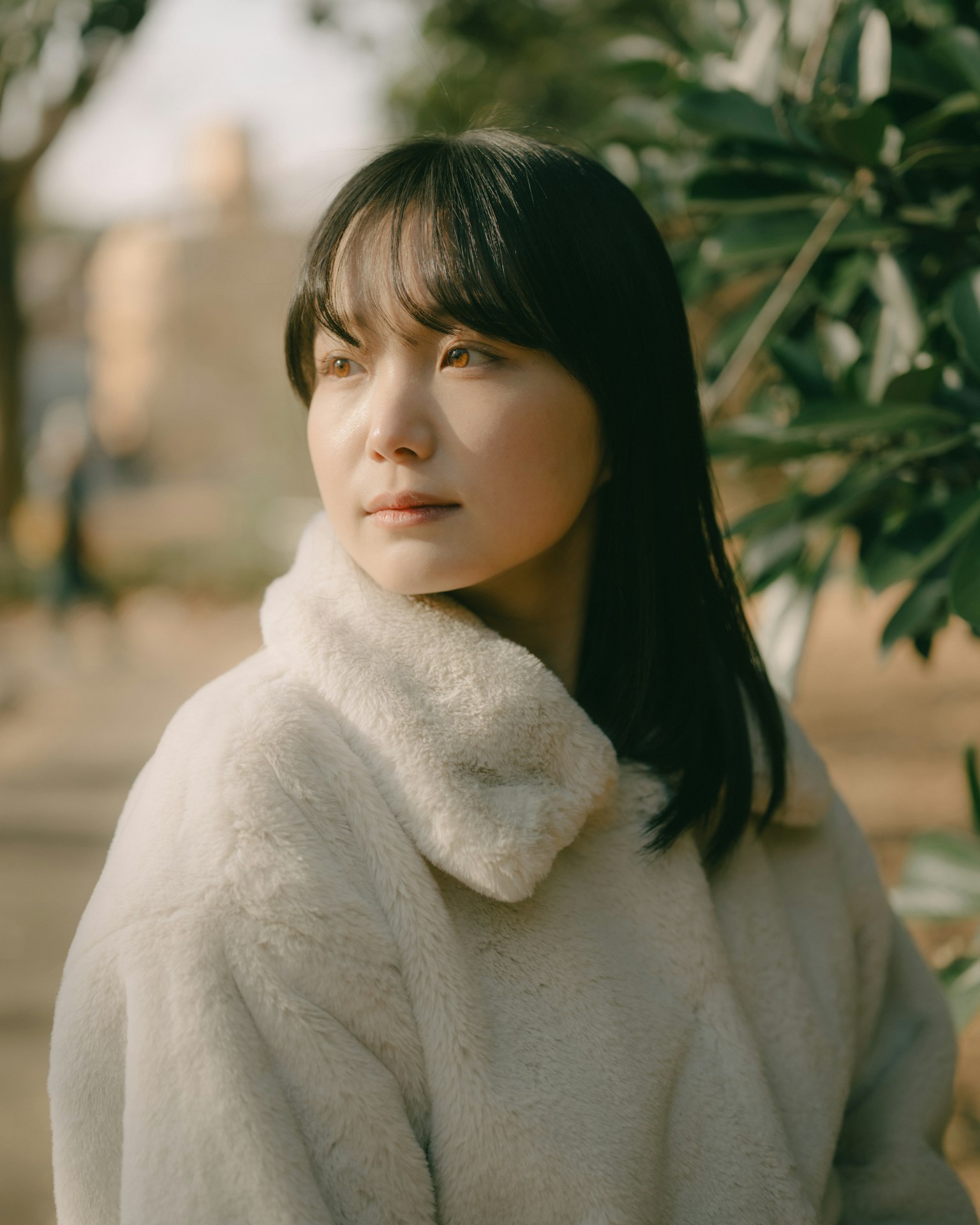 Donna in un cappotto bianco che sorride dolcemente vicino a un albero