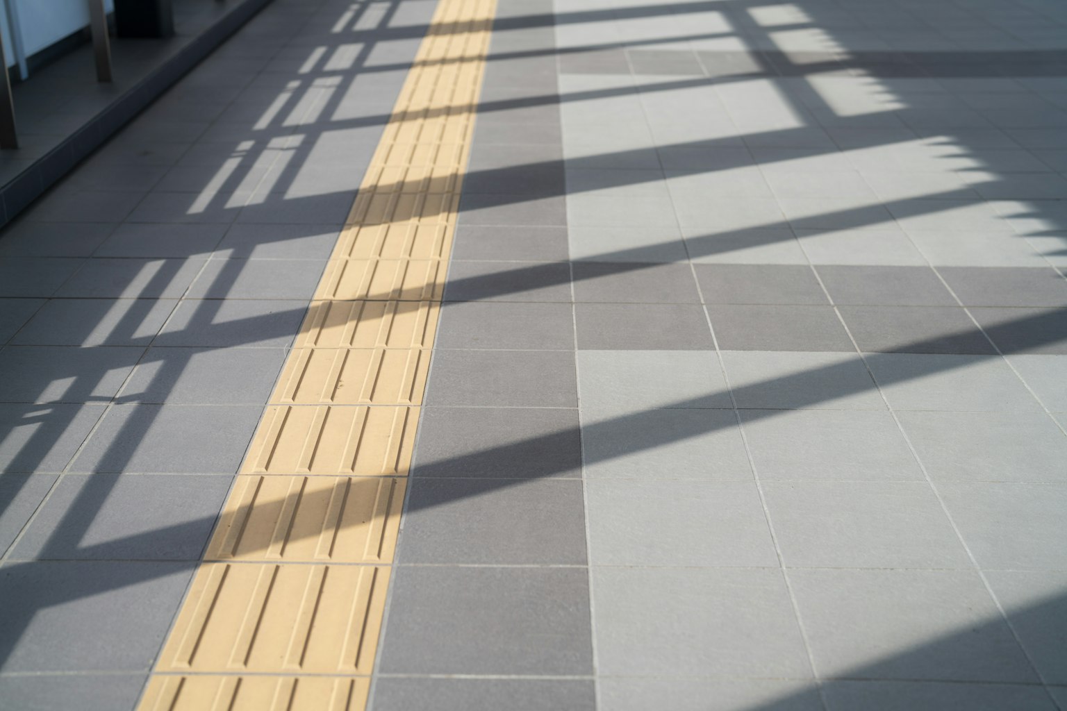 Ein Gehweg mit einer gelben Tastlinie auf hellen Fliesen und Schatten