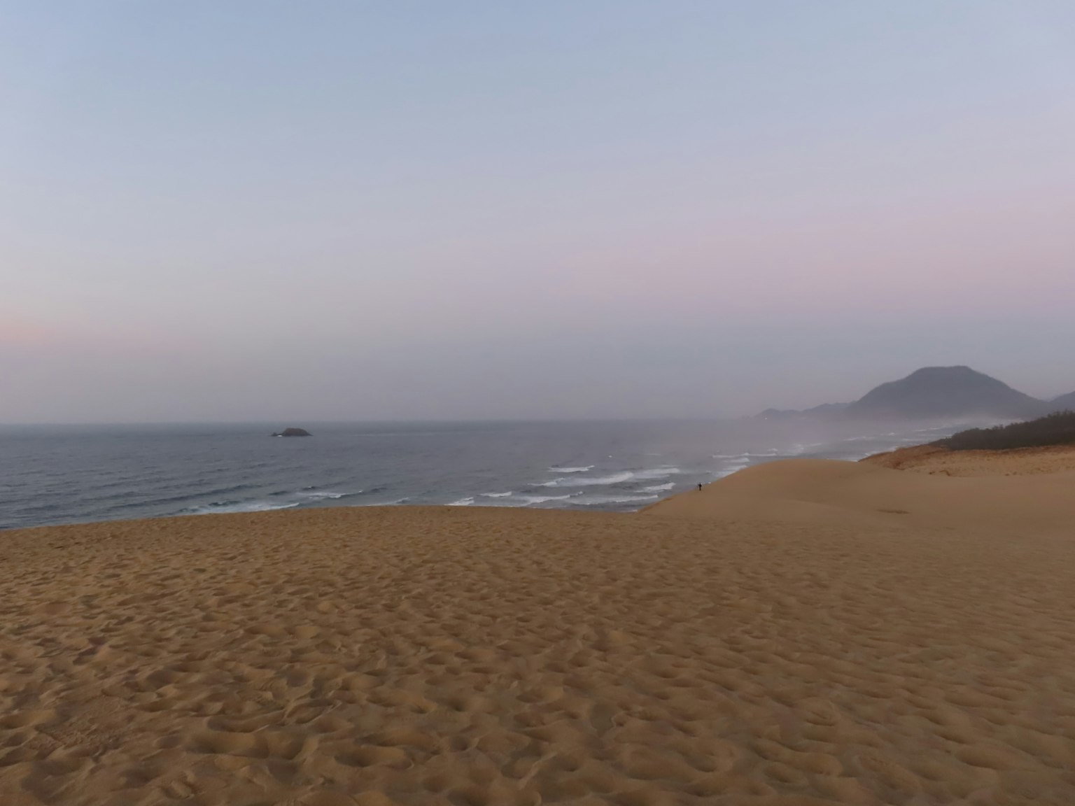 ชายหาดทรายชายฝั่งพร้อมคลื่นอ่อนสีอ่อนในท้องฟ้ายามเย็น