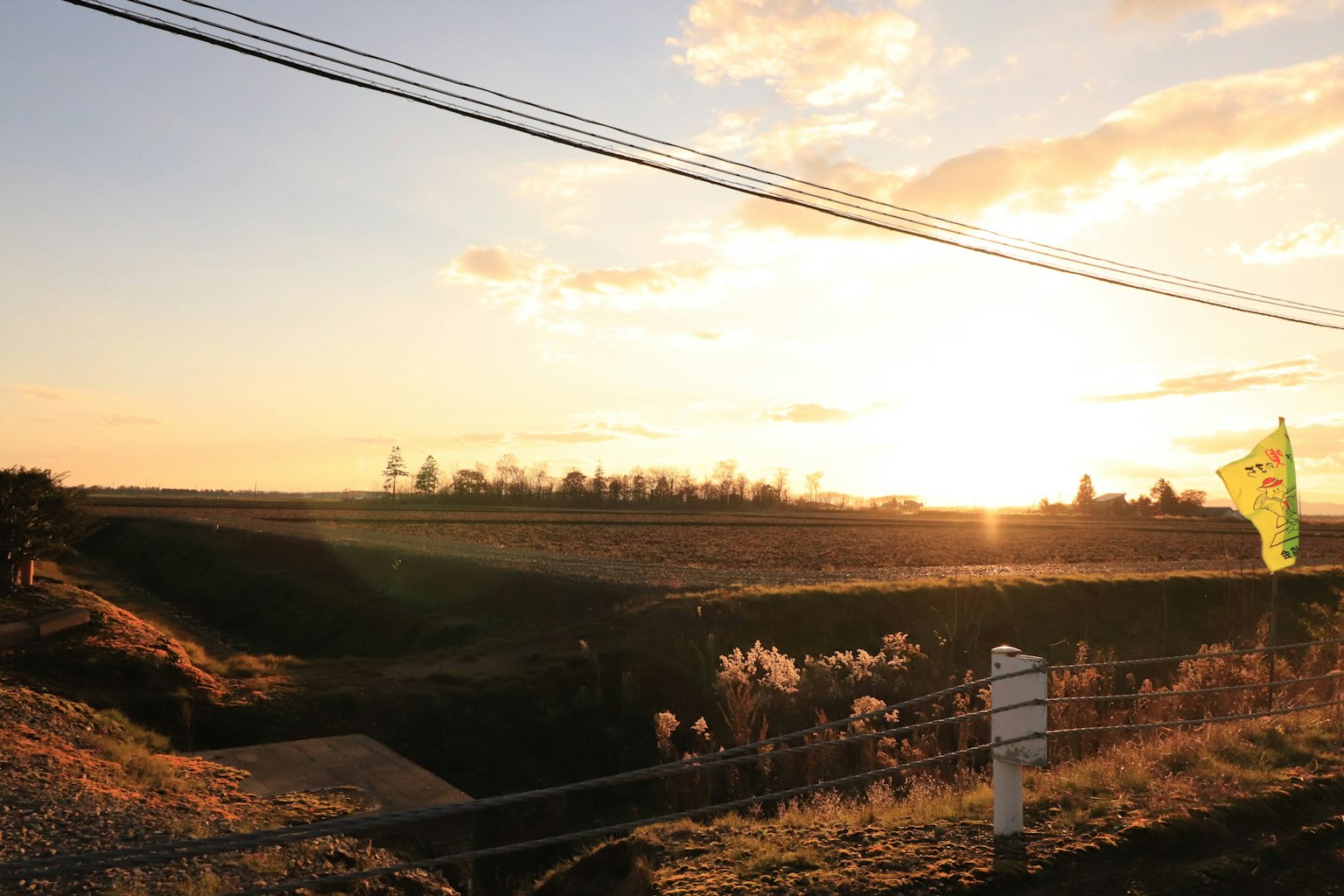 Sunset over a rural landscape with silhouettes of power lines